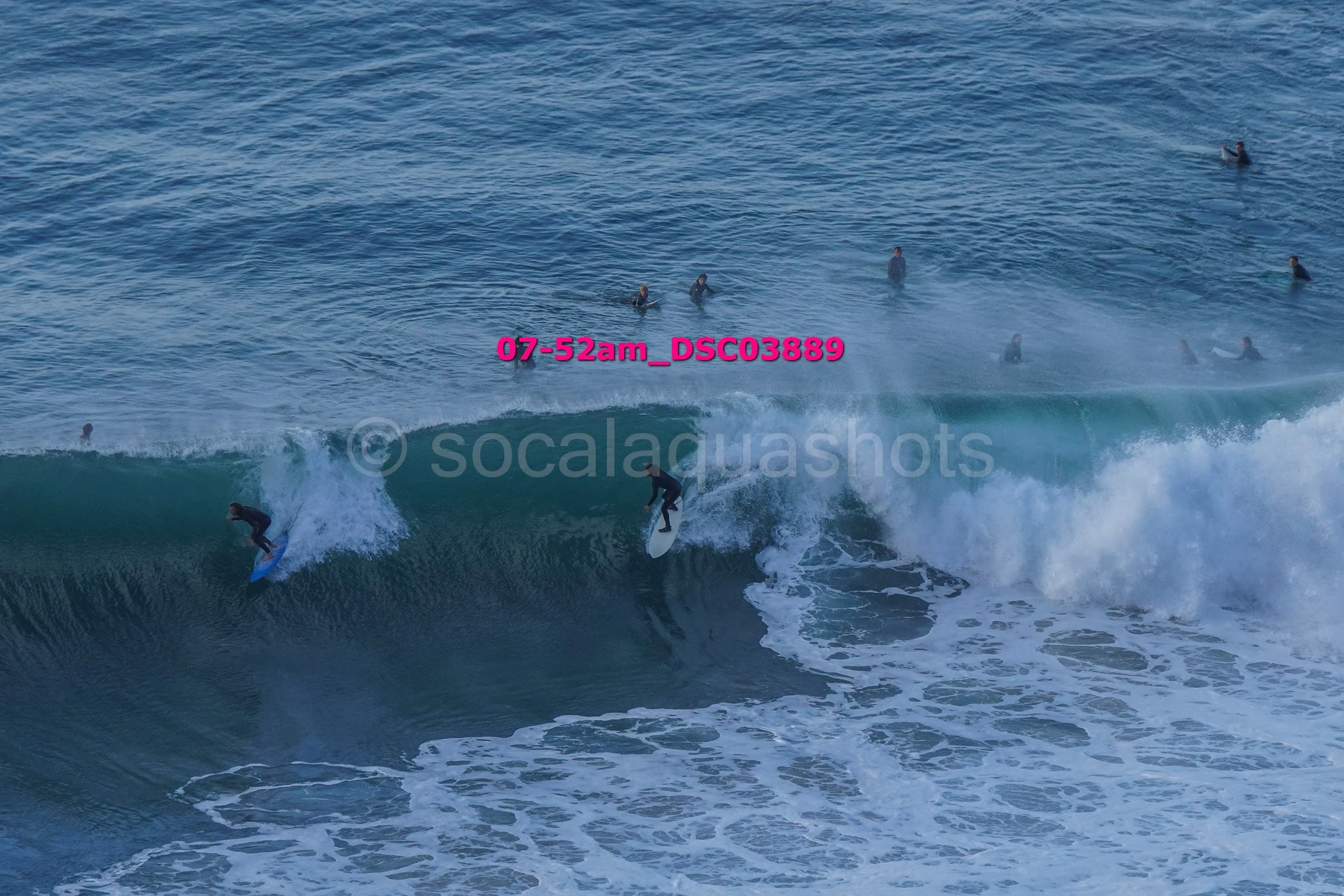 Surfers riding a wave with several people in the water in the background.