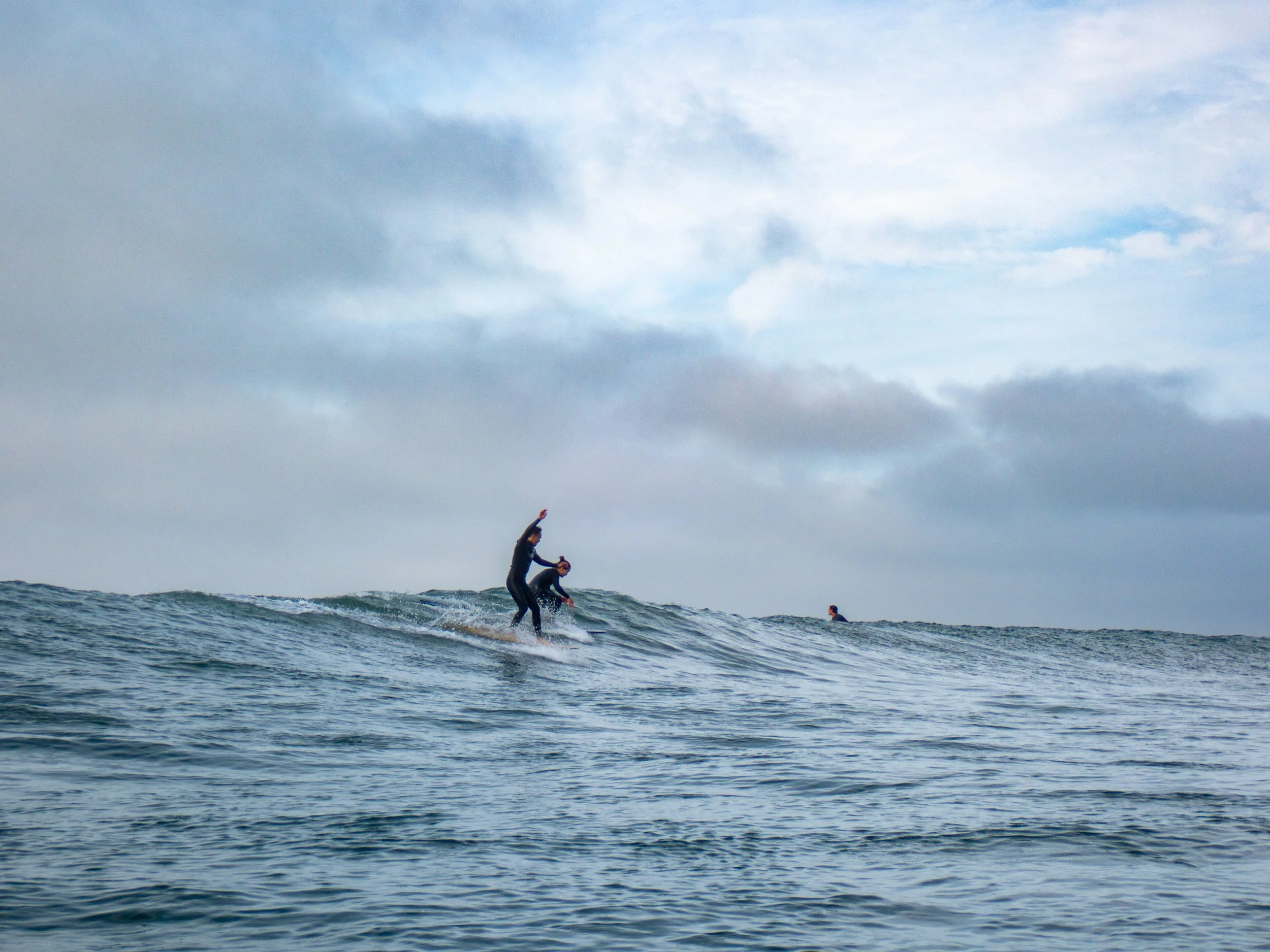 People surfing on the ocean waves under a cloudy sky.