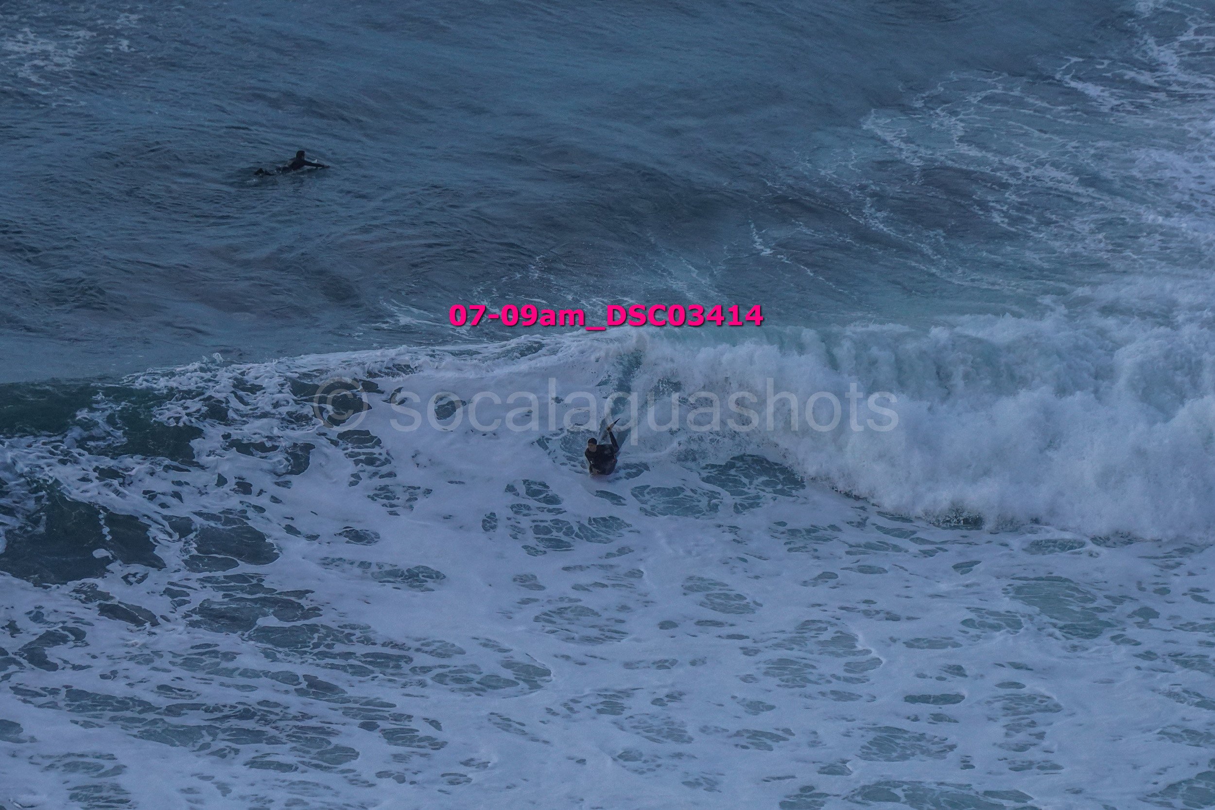 A surfer riding a wave in the ocean, with another surfer visible farther out in the water.