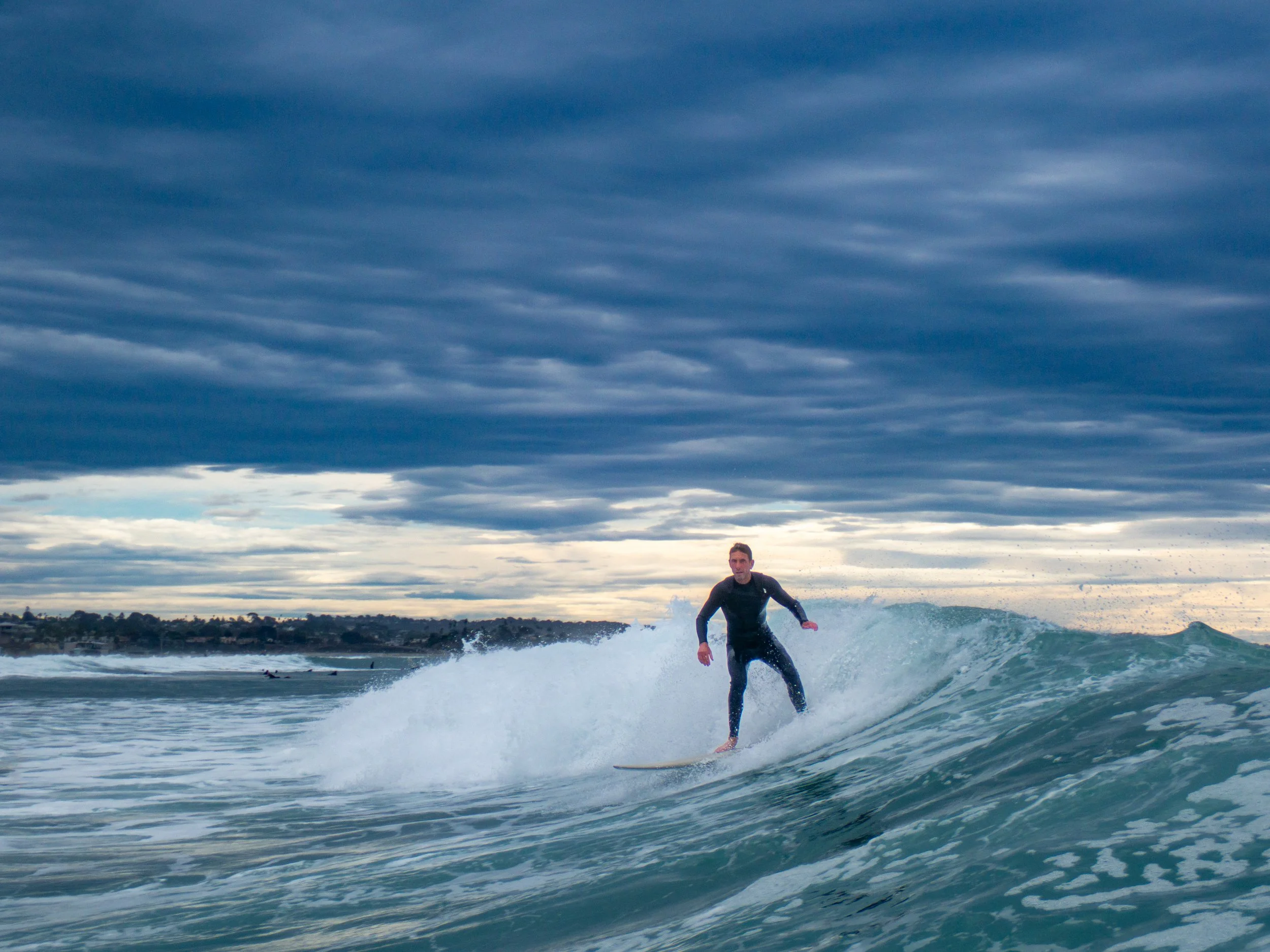 A man surfing on a wave in the ocean with a cloudy sky overhead.