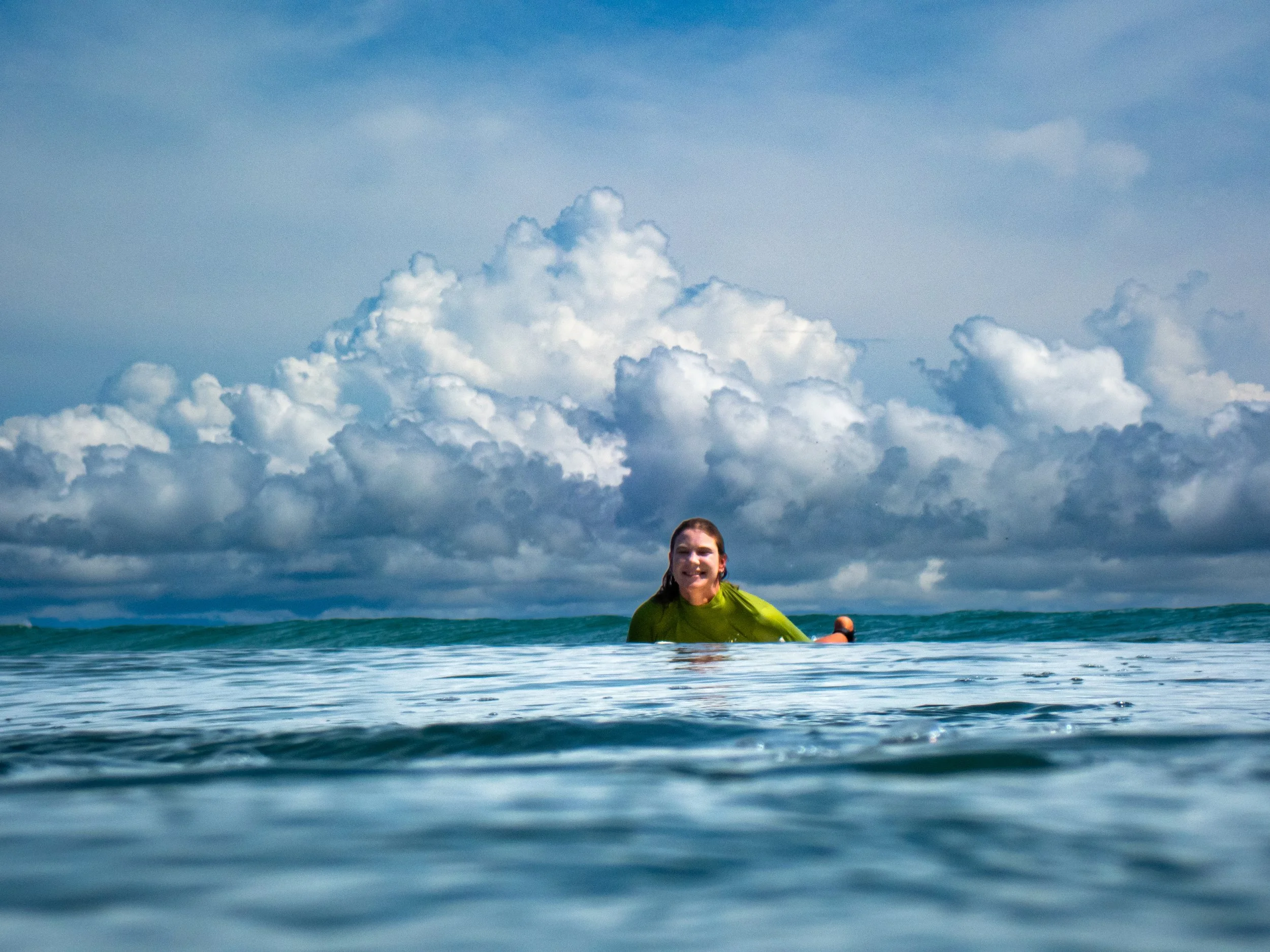 A woman in a yellow shirt swimming in the ocean with a cloudy sky above.