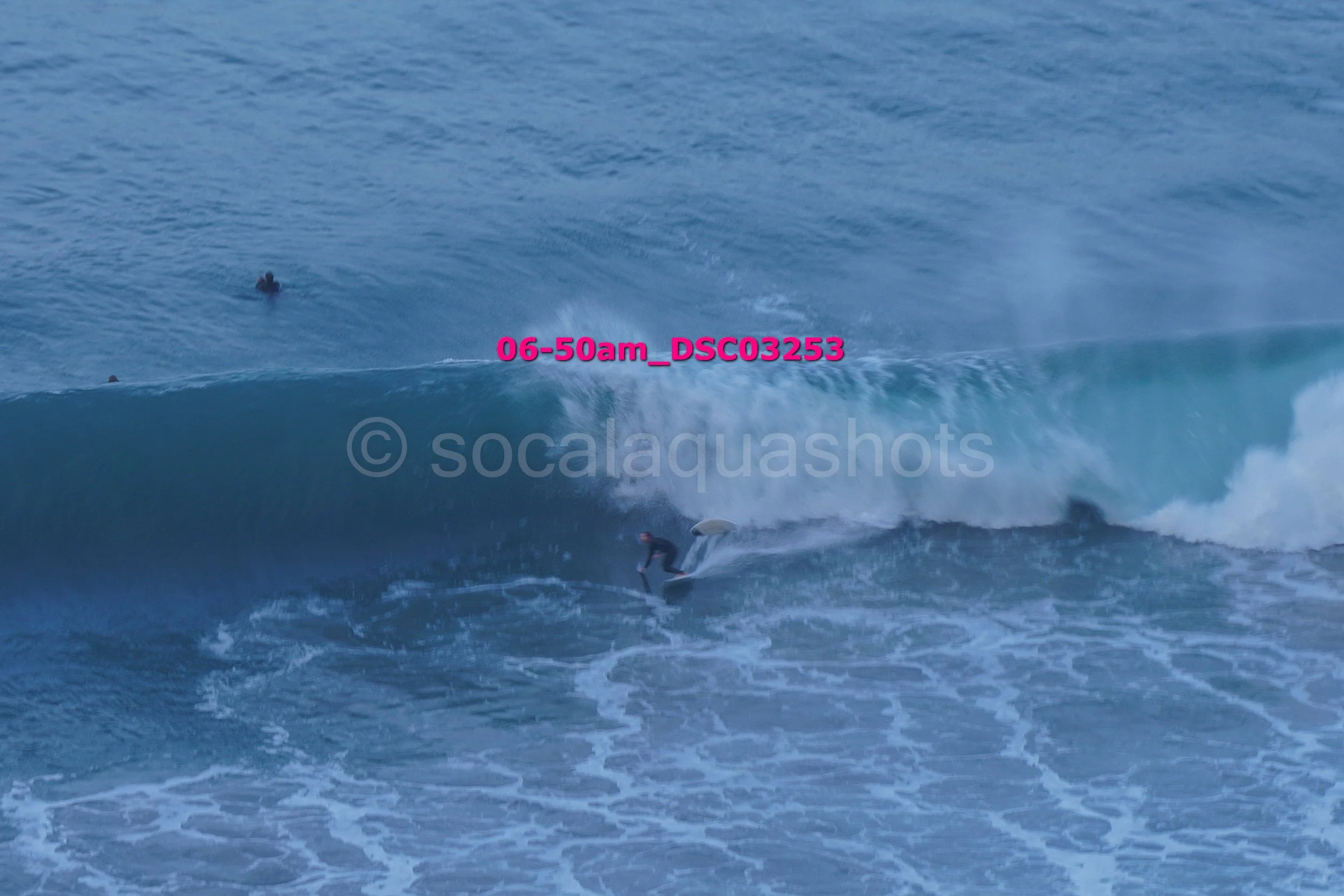 Surfer riding a large ocean wave with another surfer in the water nearby.