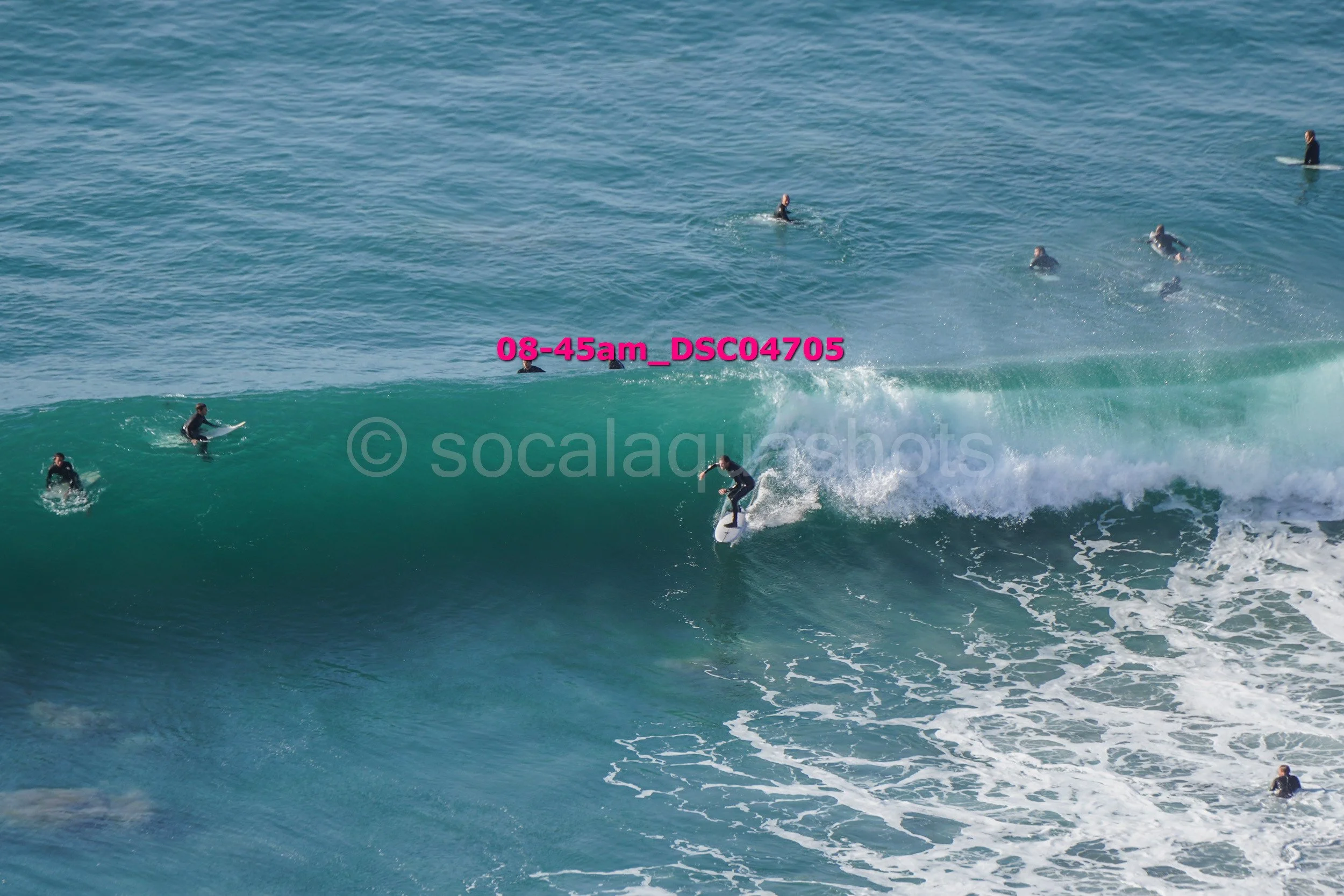 Surfer riding a wave with several surfers and paddleboarders in the water around him.