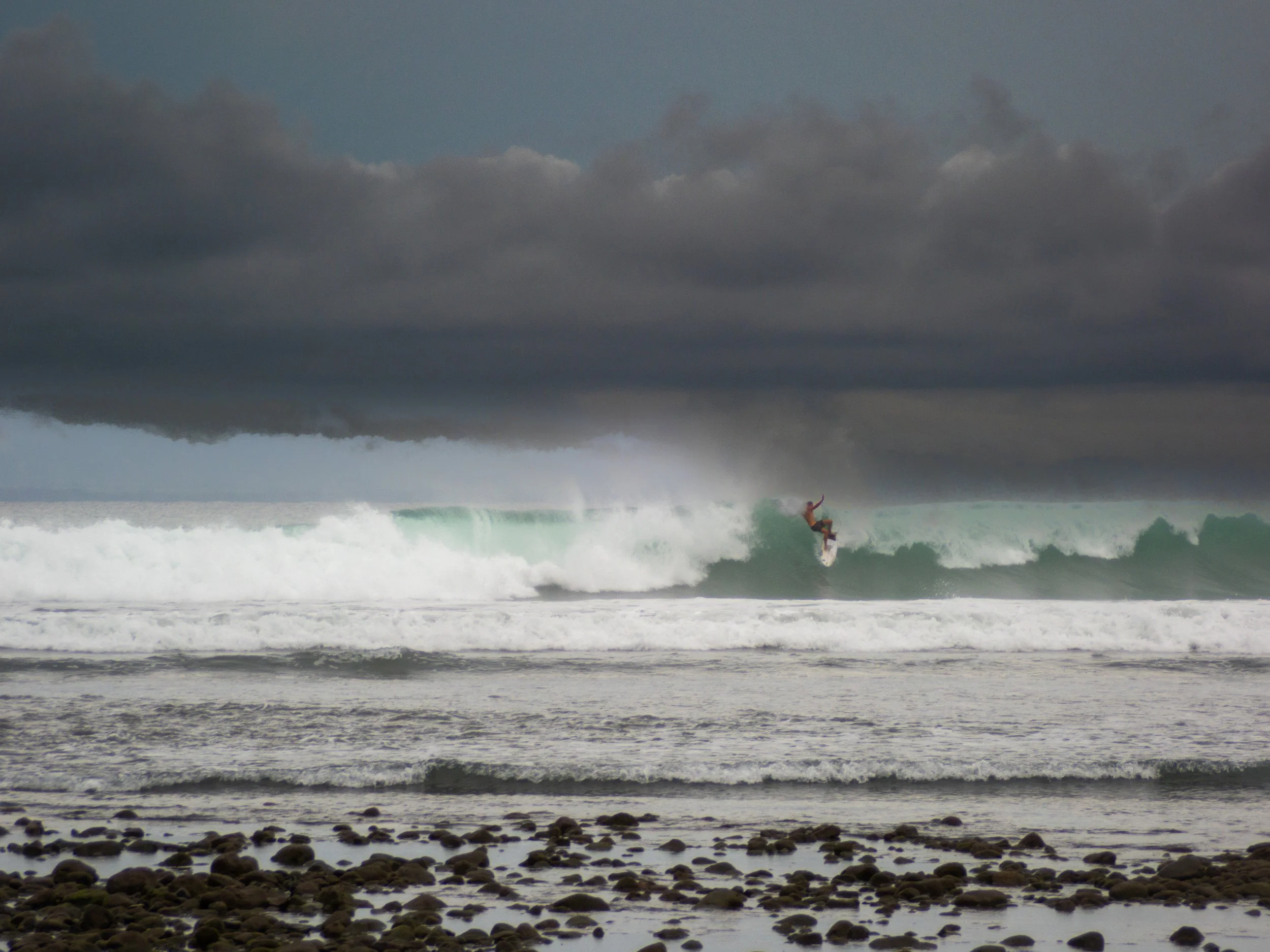 Surfer riding large wave under dark cloudy sky
