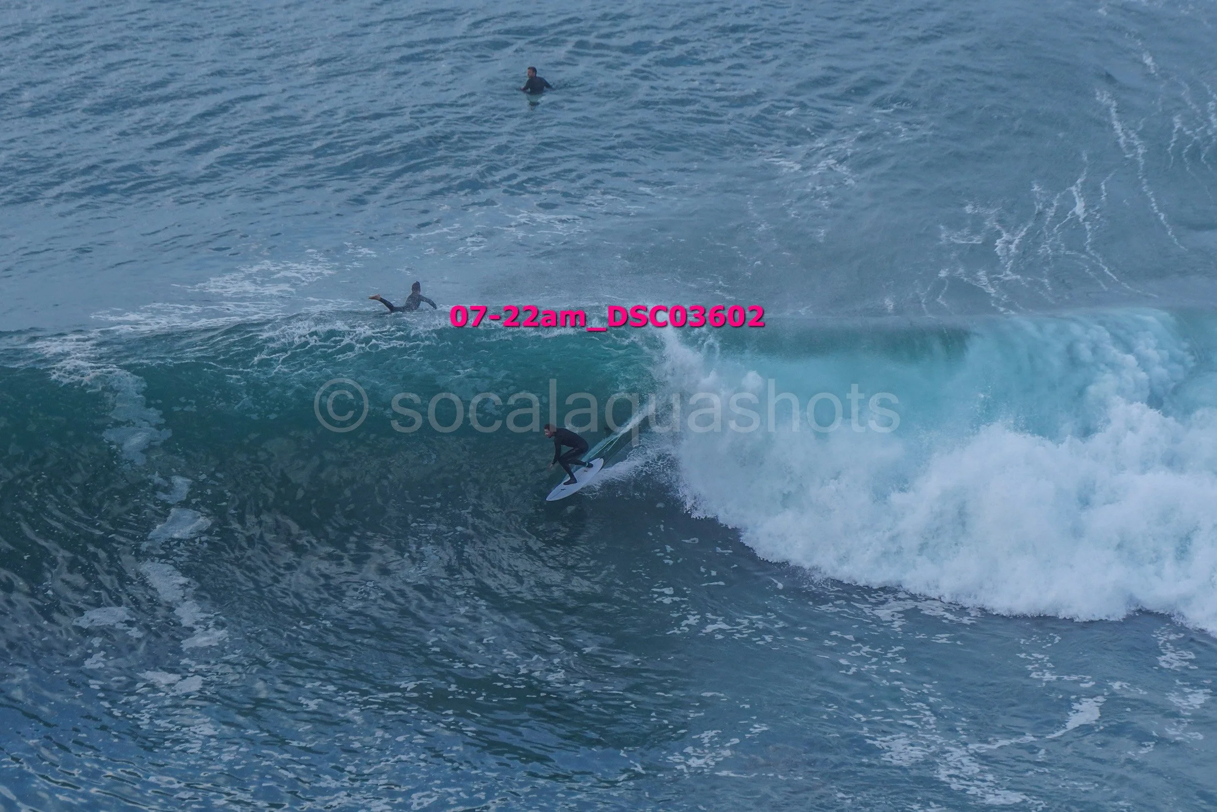 Surfer riding a wave with two other surfers in the water nearby.