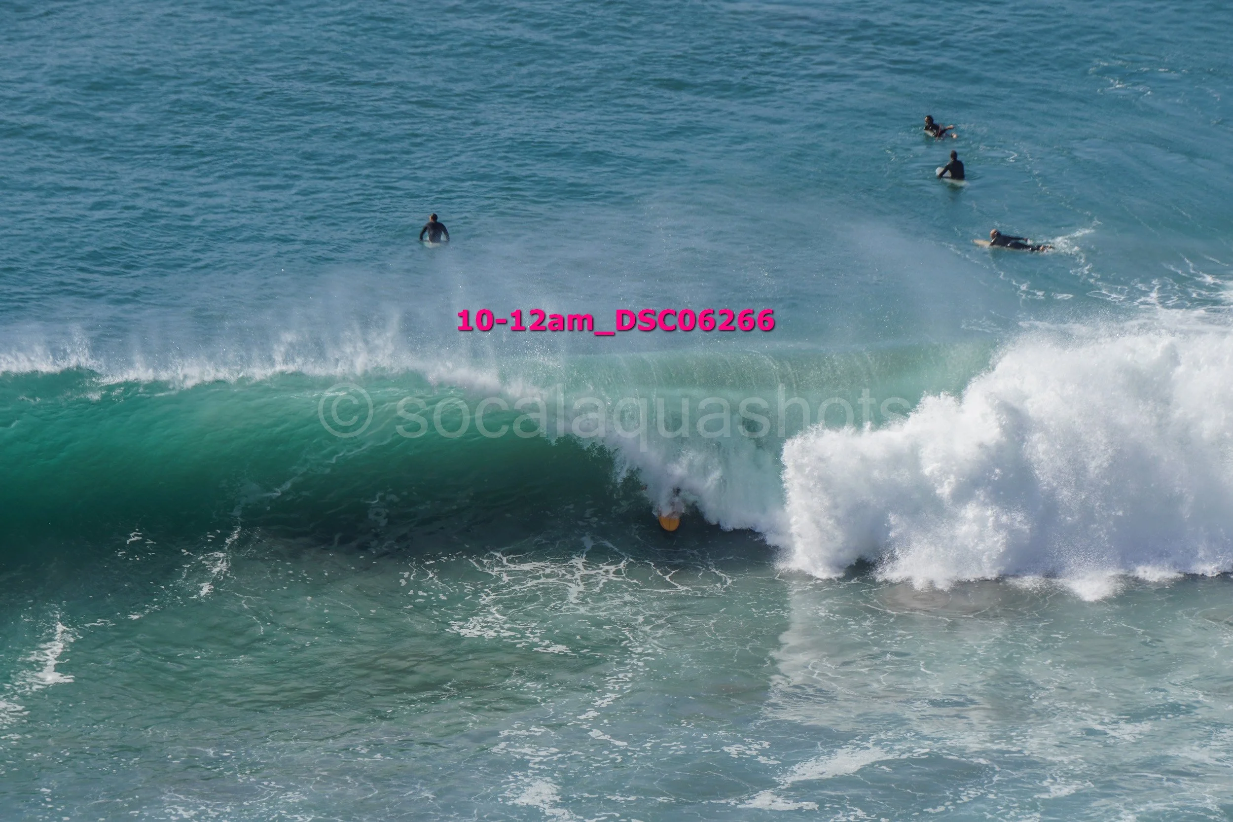 People surfing and swimming in the ocean; large wave in foreground