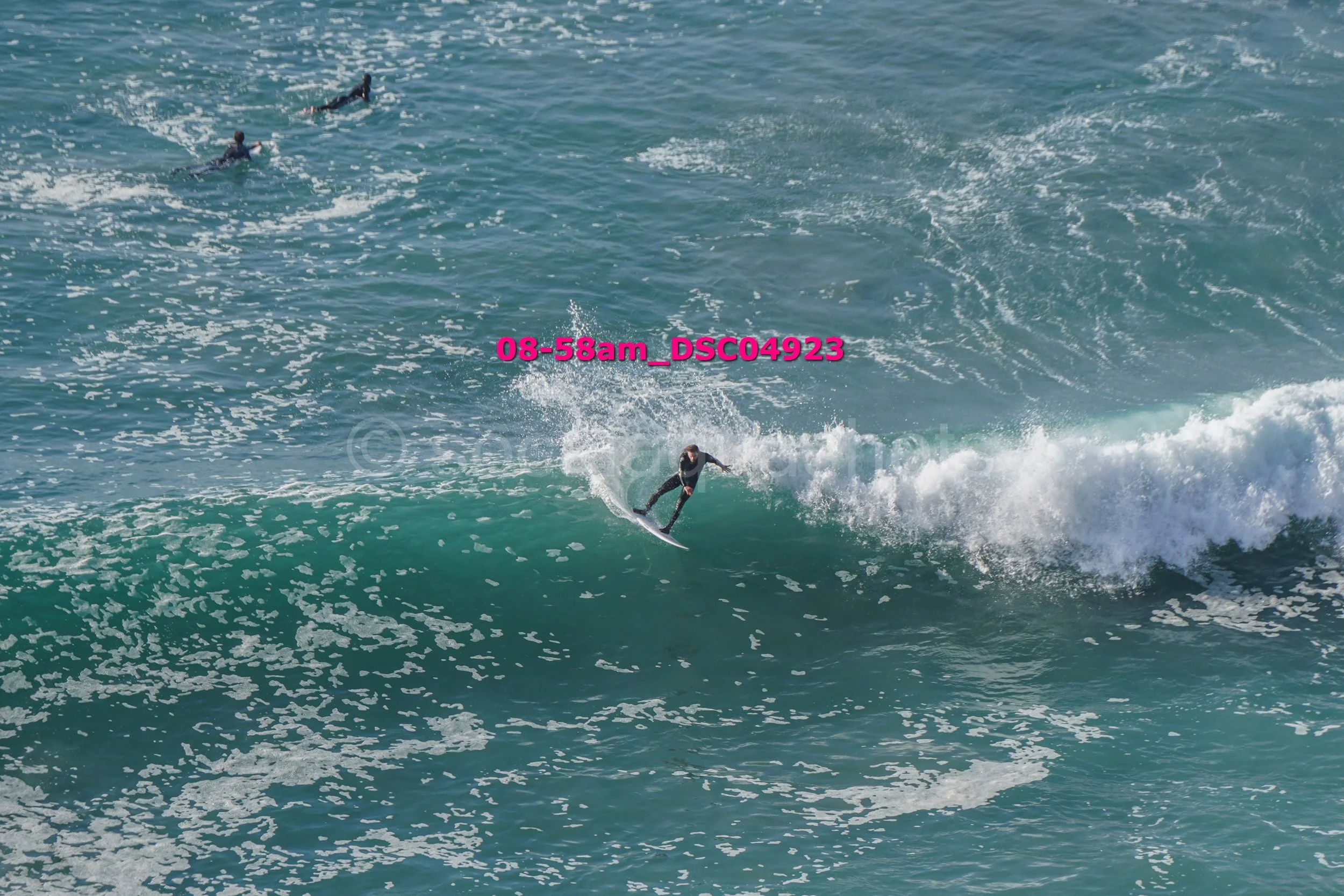 A surfer riding a wave in the ocean with two other surfers visible in the background.