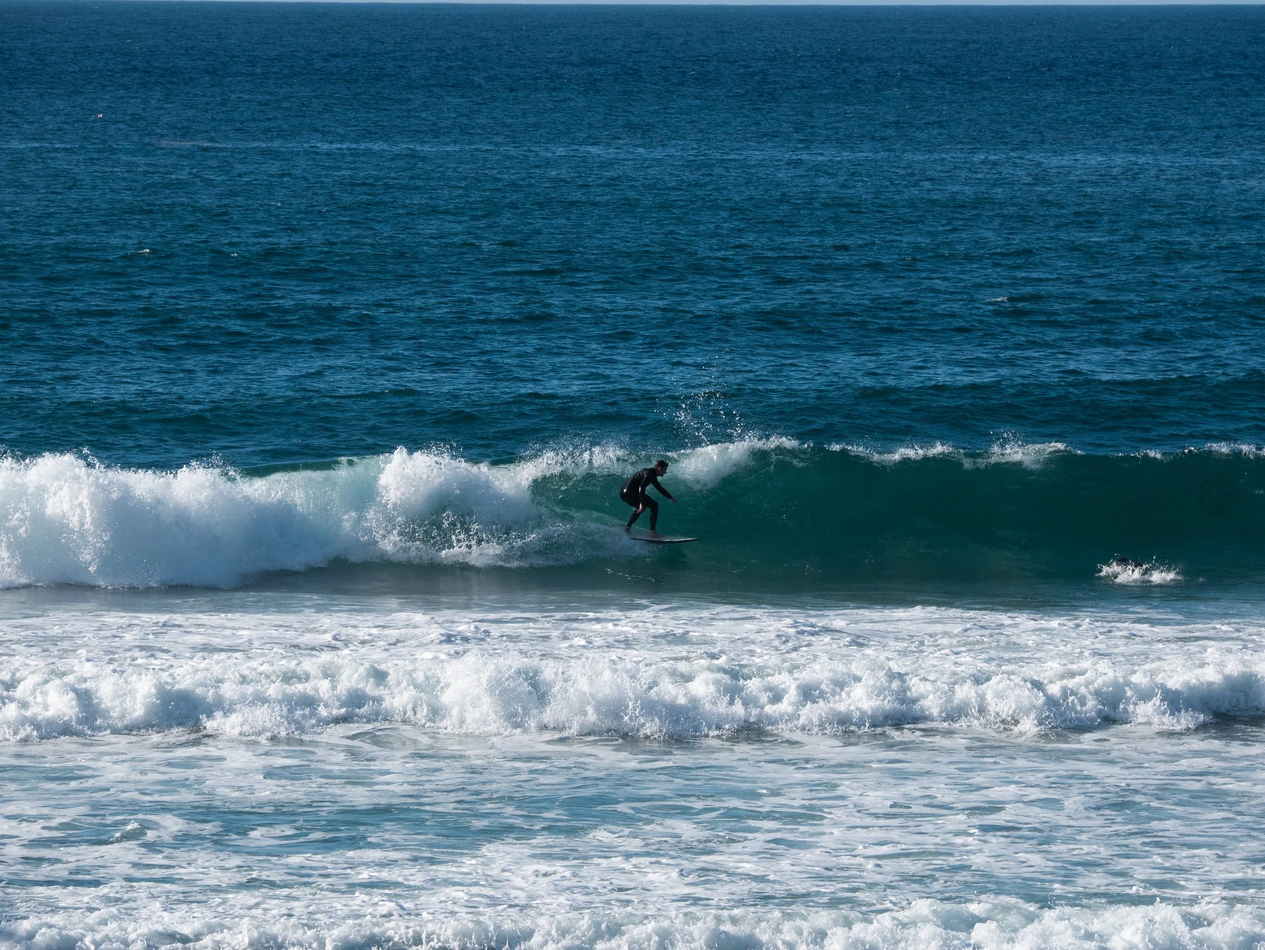 Person surfing on a wave in the ocean under a clear sky.