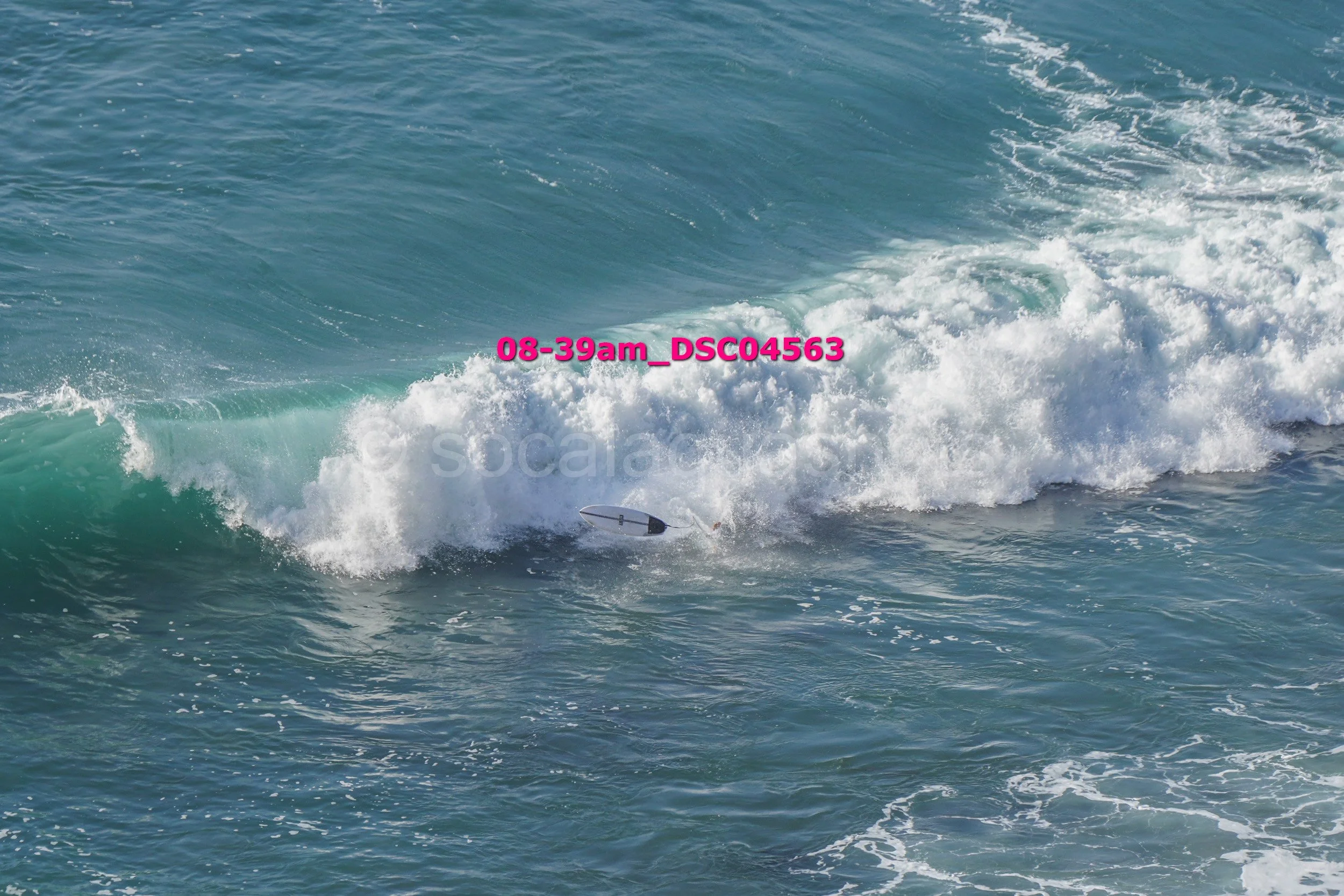 Ocean waves with a small surfboard partially submerged near the crest of a wave, with pink text overlay reading '08-39am_DSC04563'.