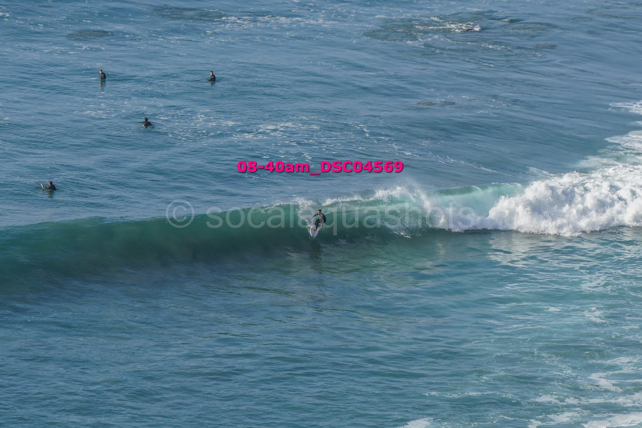 Surfer riding a wave in the ocean with five other surfers in the water nearby.