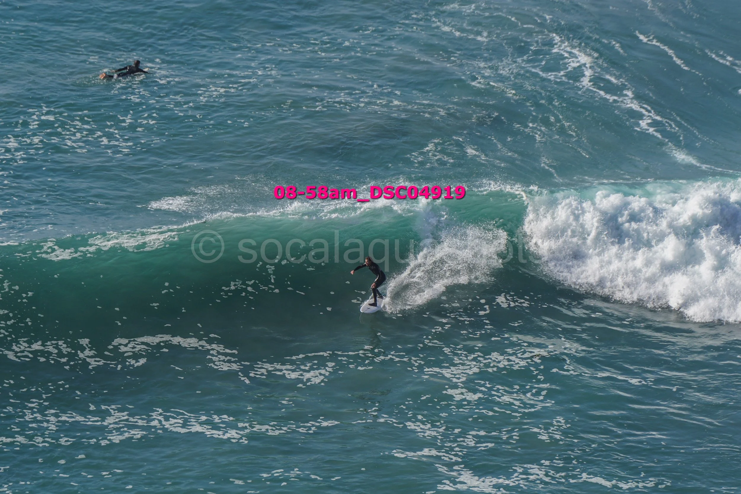 A person surfing on a wave in the ocean with another person swimming in the water nearby.
