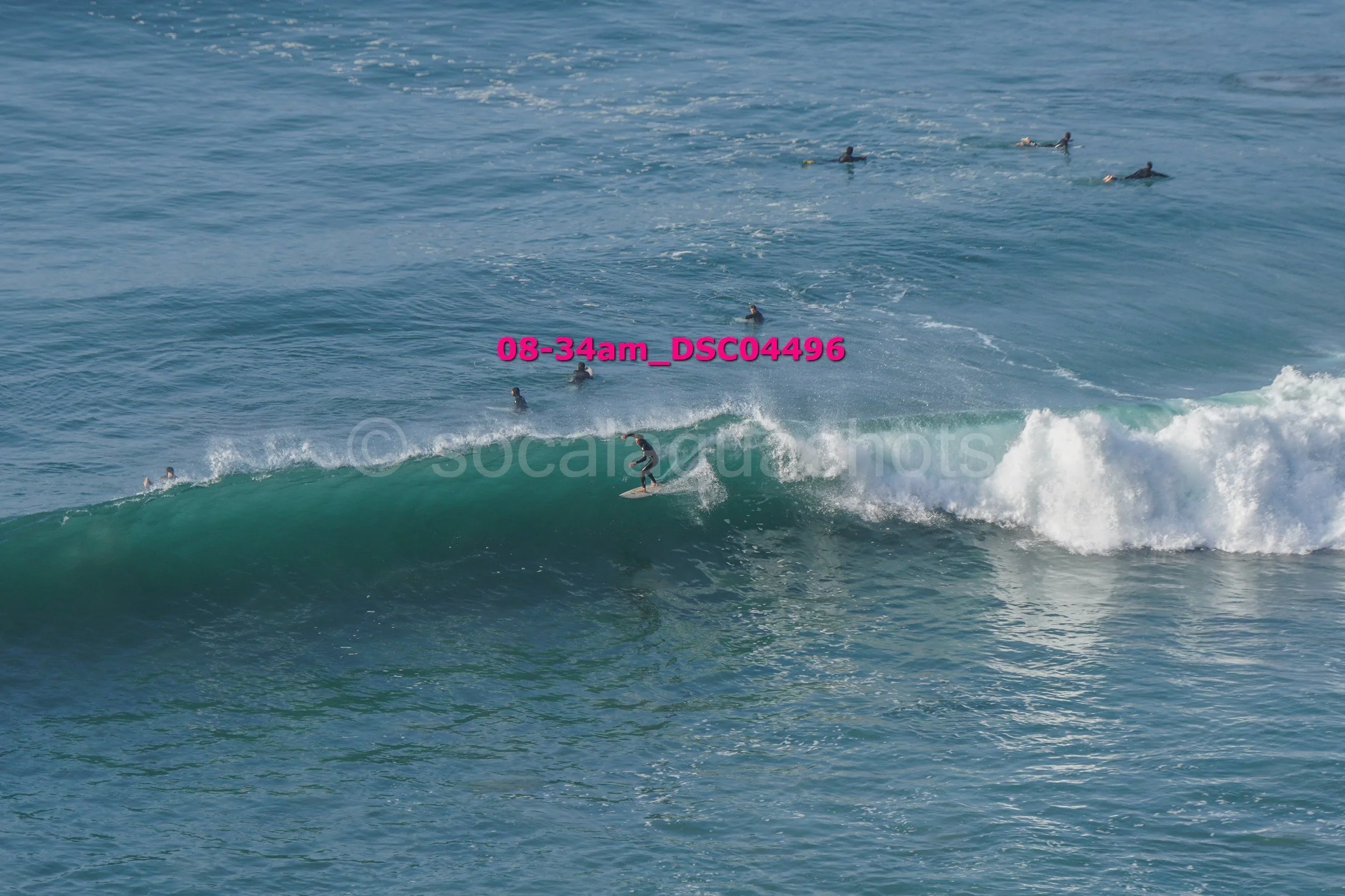 A surfer riding a wave with several people swimming in the ocean nearby.