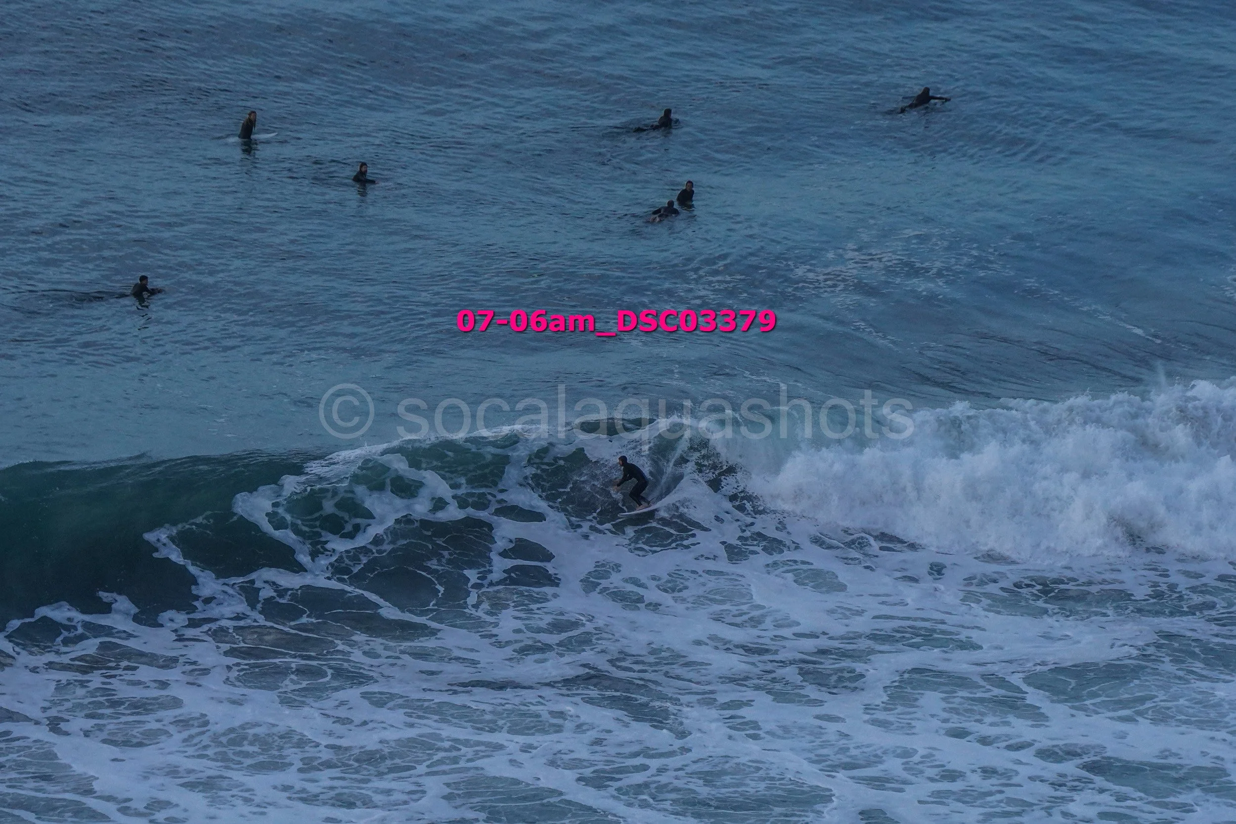 Surfer riding a wave while several people swim in the ocean in the background.