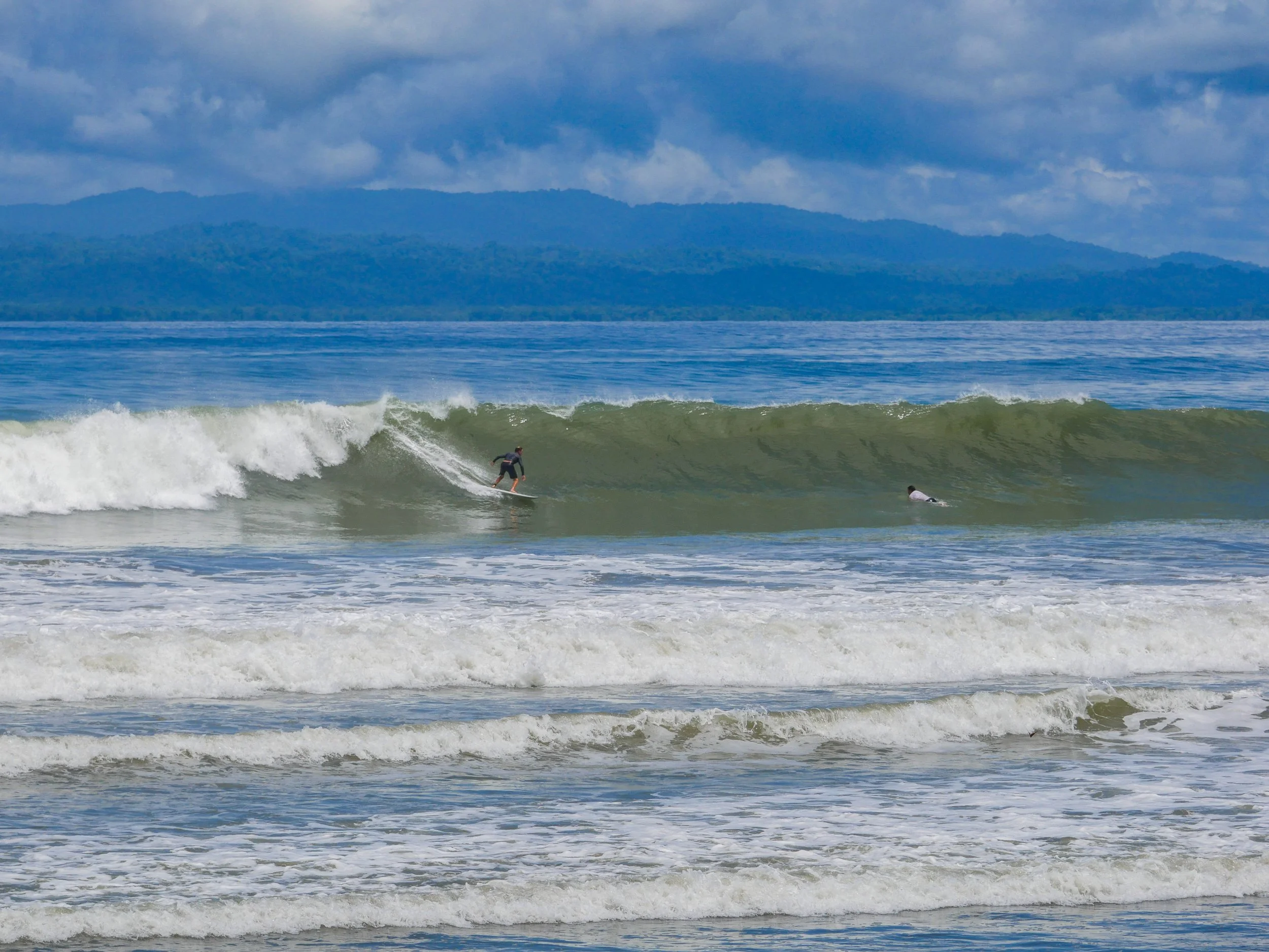 Surfer riding a wave in the ocean with mountains in the background