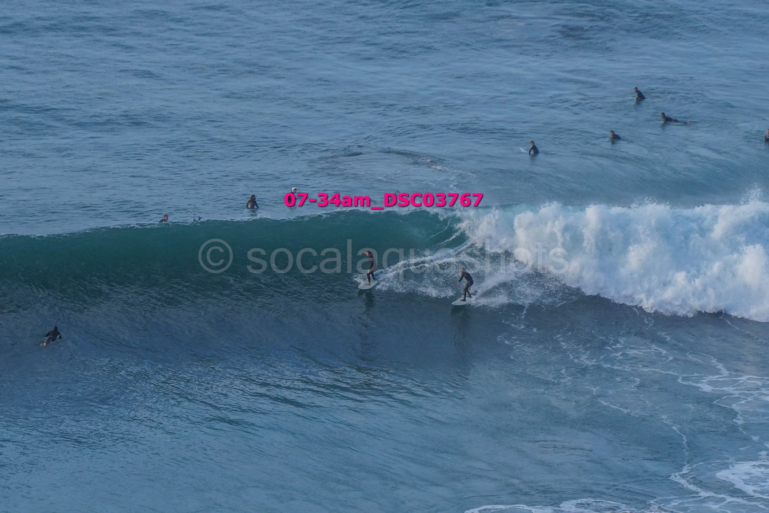 Surfers riding and waiting for waves in the ocean with some surfers swimming nearby.