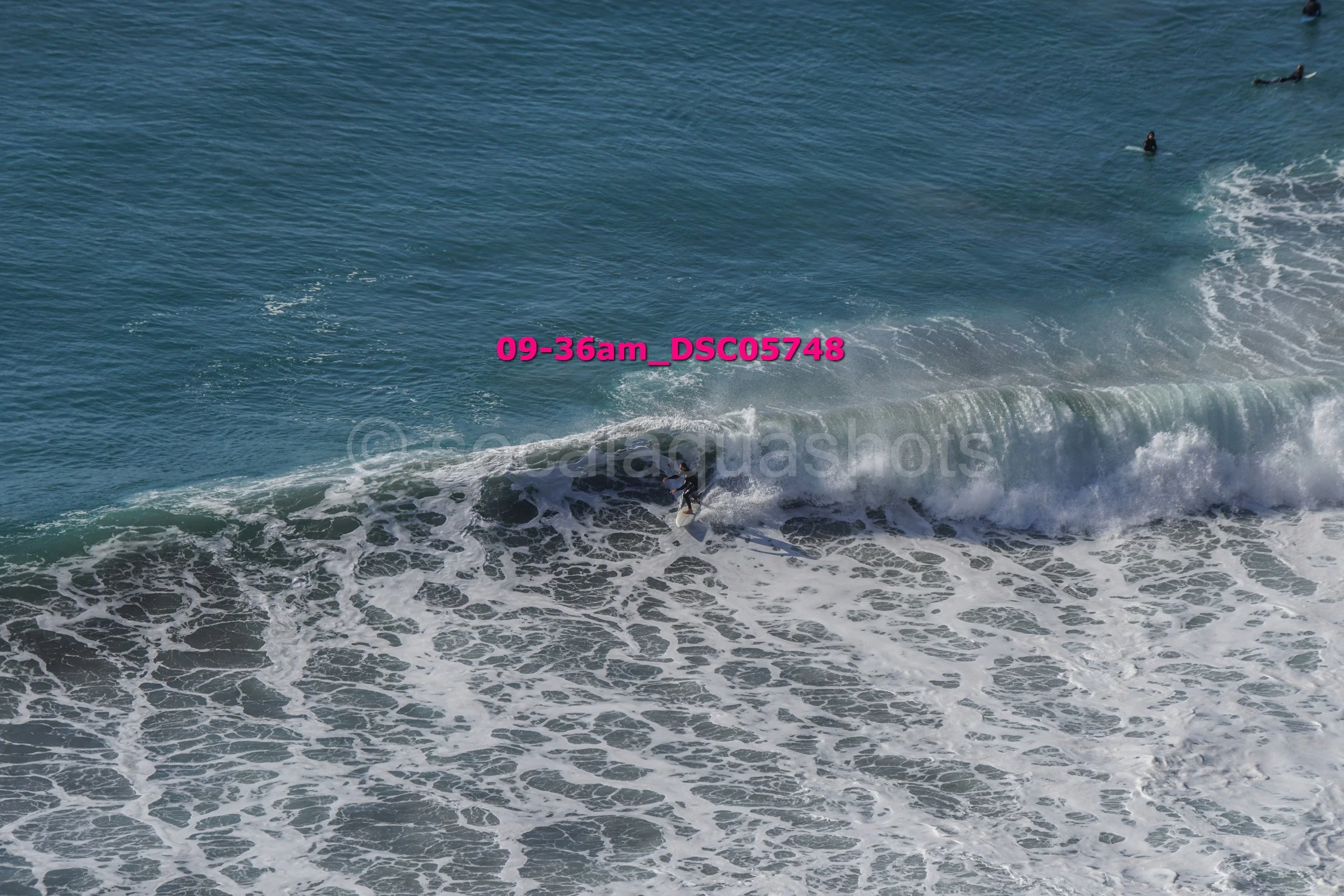 A surfer riding a wave in the ocean as other surfers wait further out in the water.
