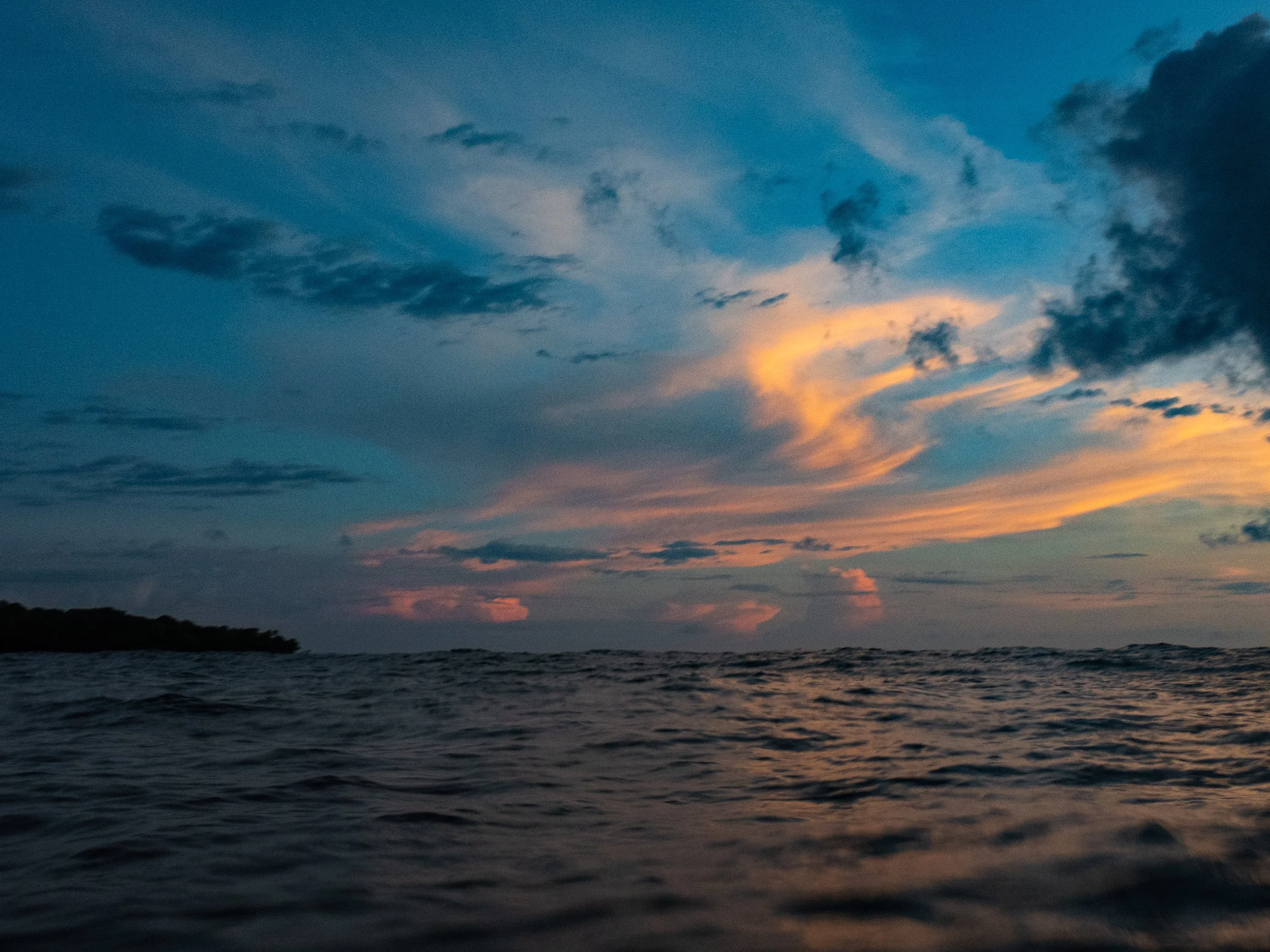 A sunset over the ocean with dark clouds in the sky and a silhouette of land in the distance.