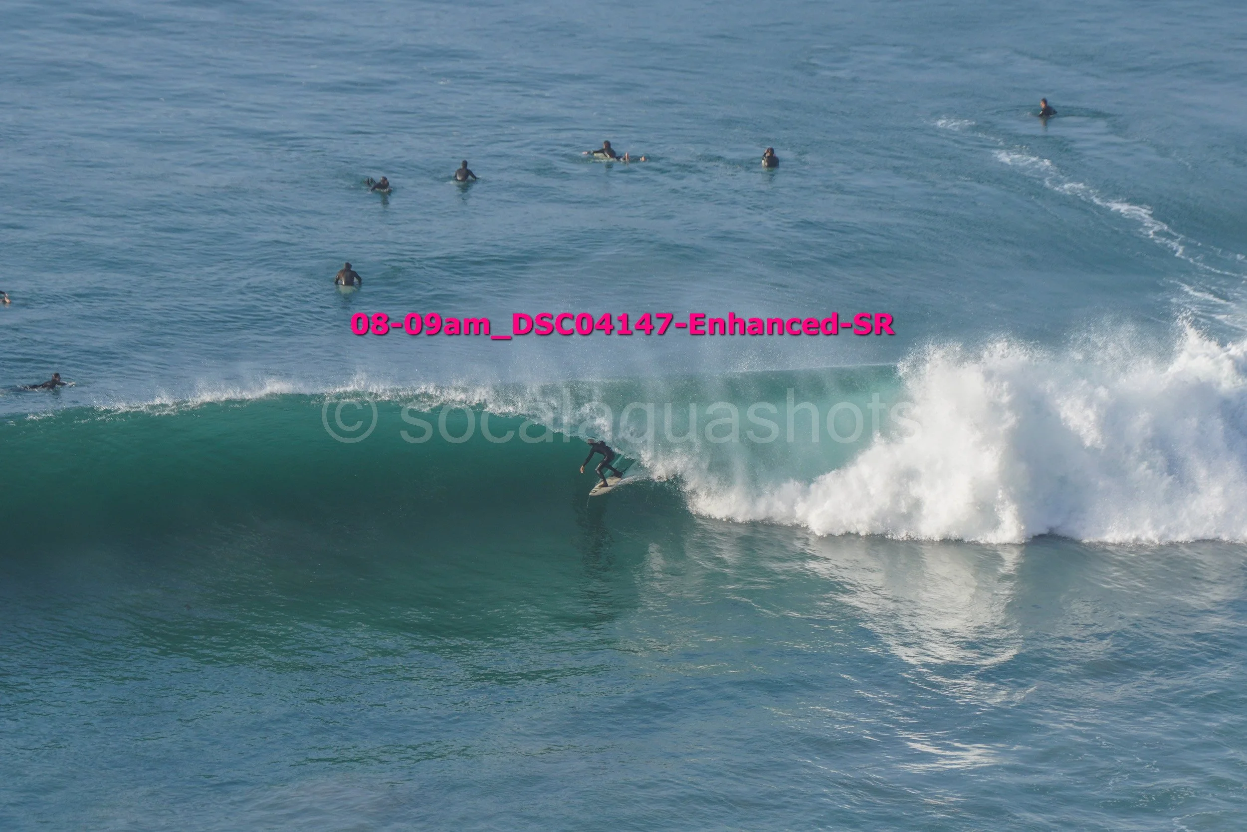 Surfer riding a wave with several swimmers in the water nearby.