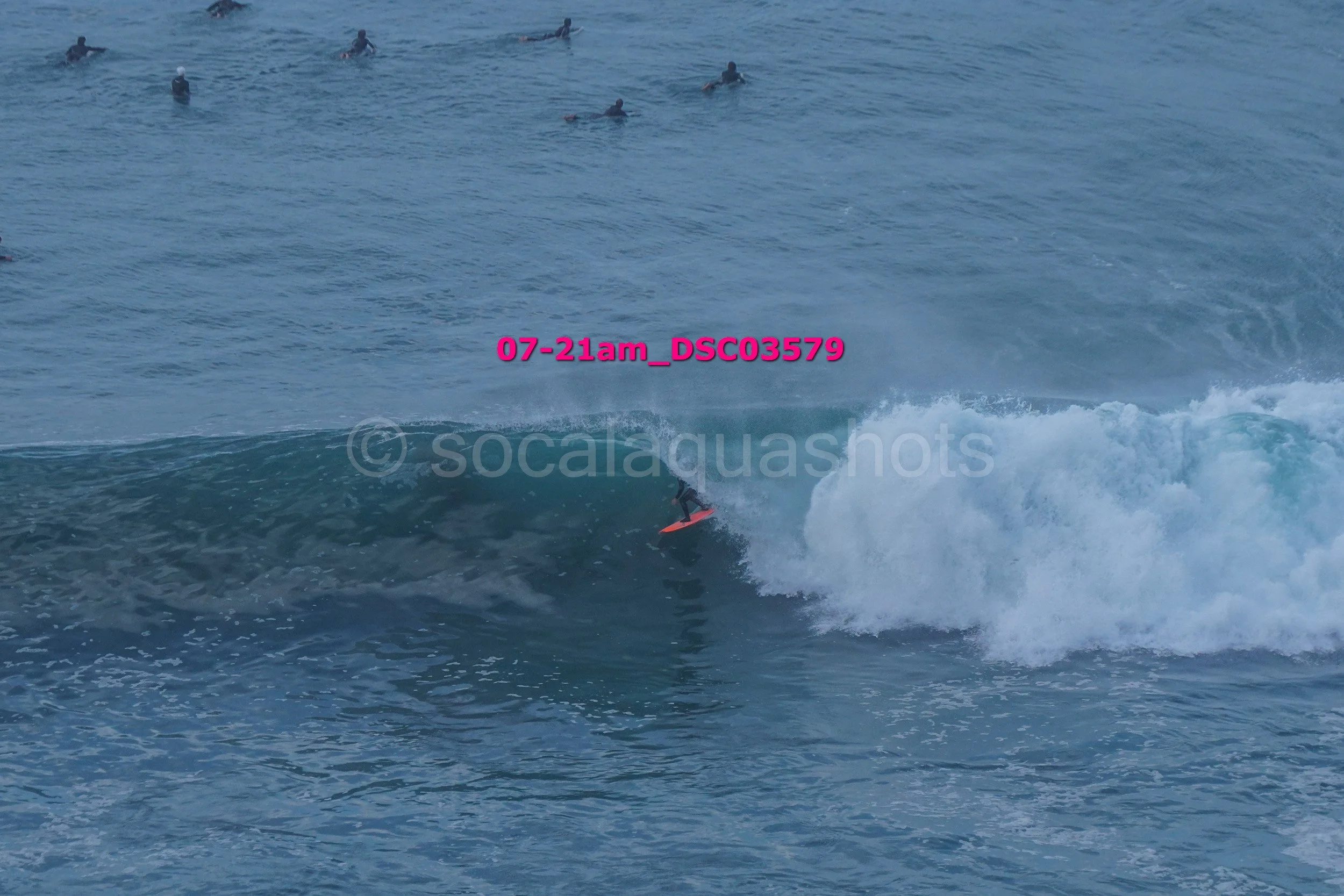A person surfing on a wave in the ocean with a group of surfers in the background