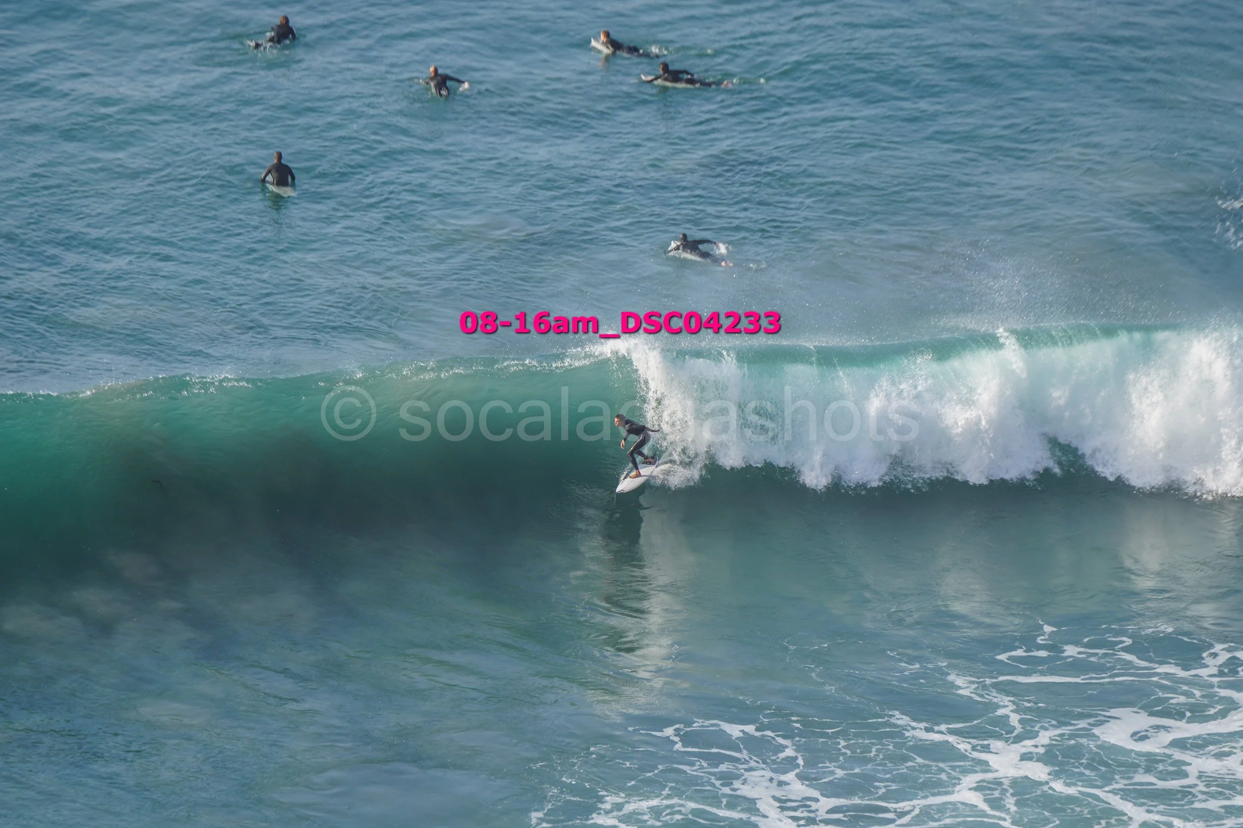 A person surfing on a wave with several people swimming and floating in the water nearby.