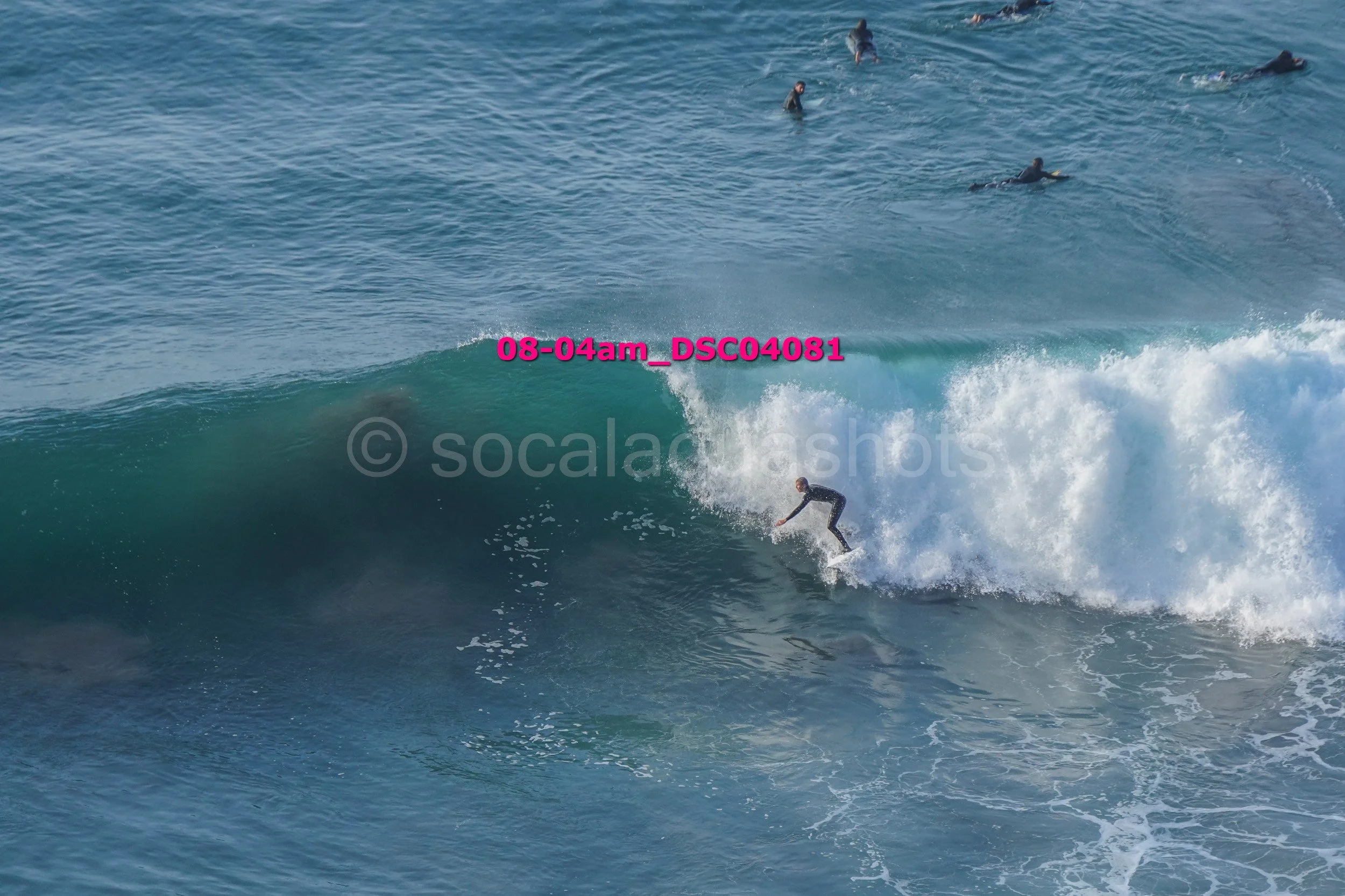 A person surfing on a wave in the ocean with other surfers visible in the background.