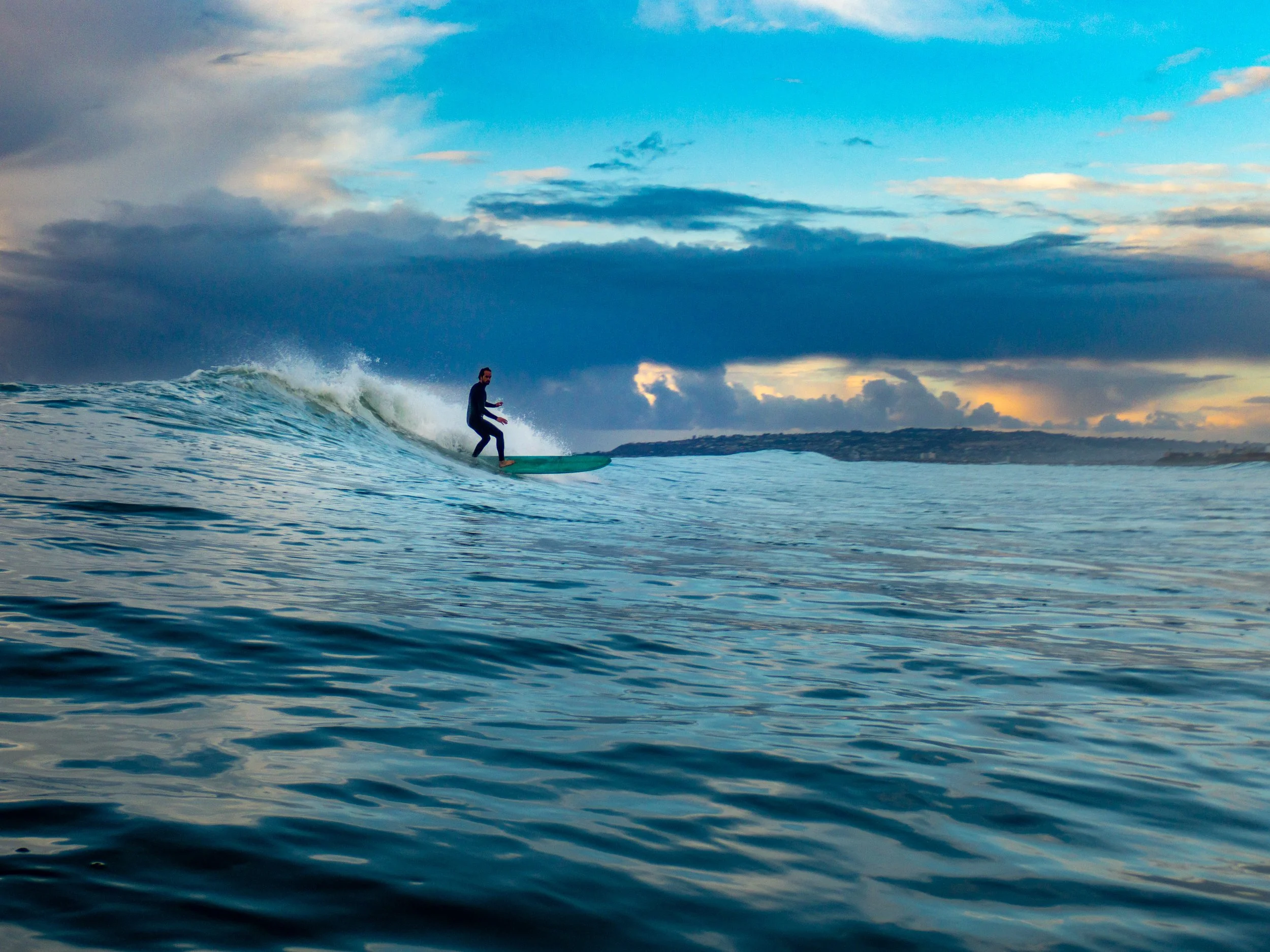 A person surfing on a wave in the ocean during sunset with a cloudy sky.