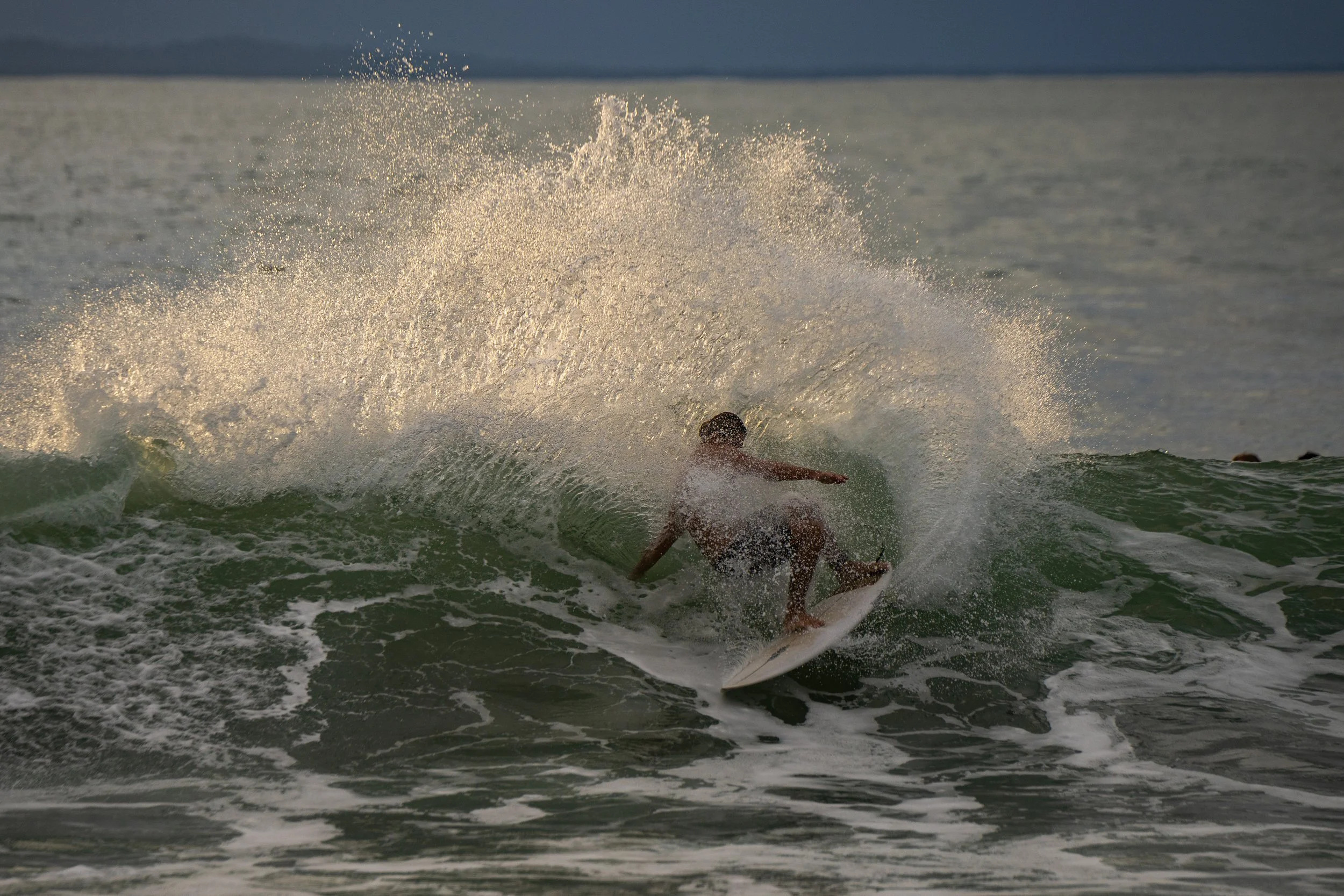 A person surfing on a wave in the ocean, splashing water as they ride the surfboard under a dark sky.
