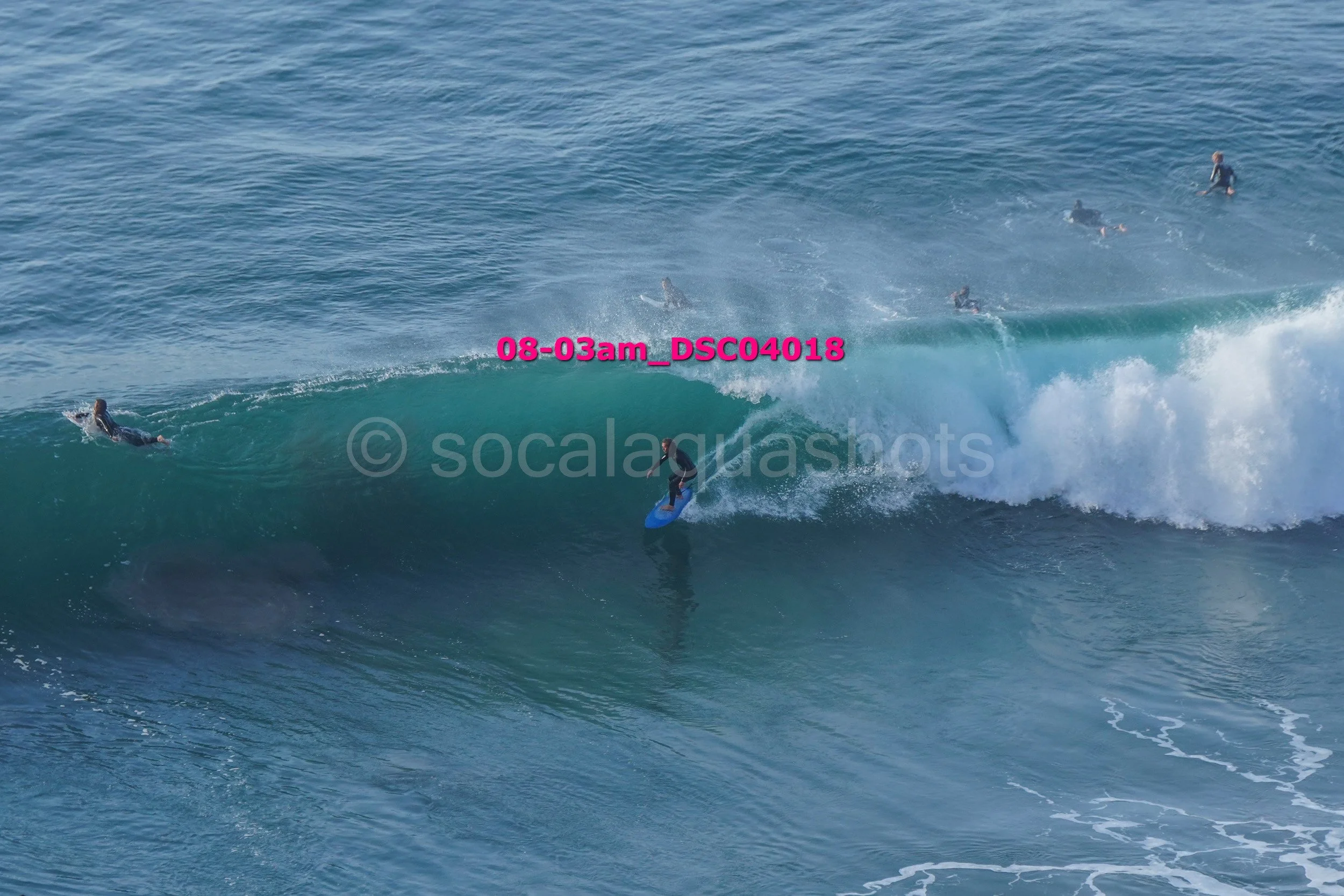 Surfer riding a wave with multiple surfers in the water in the background.
