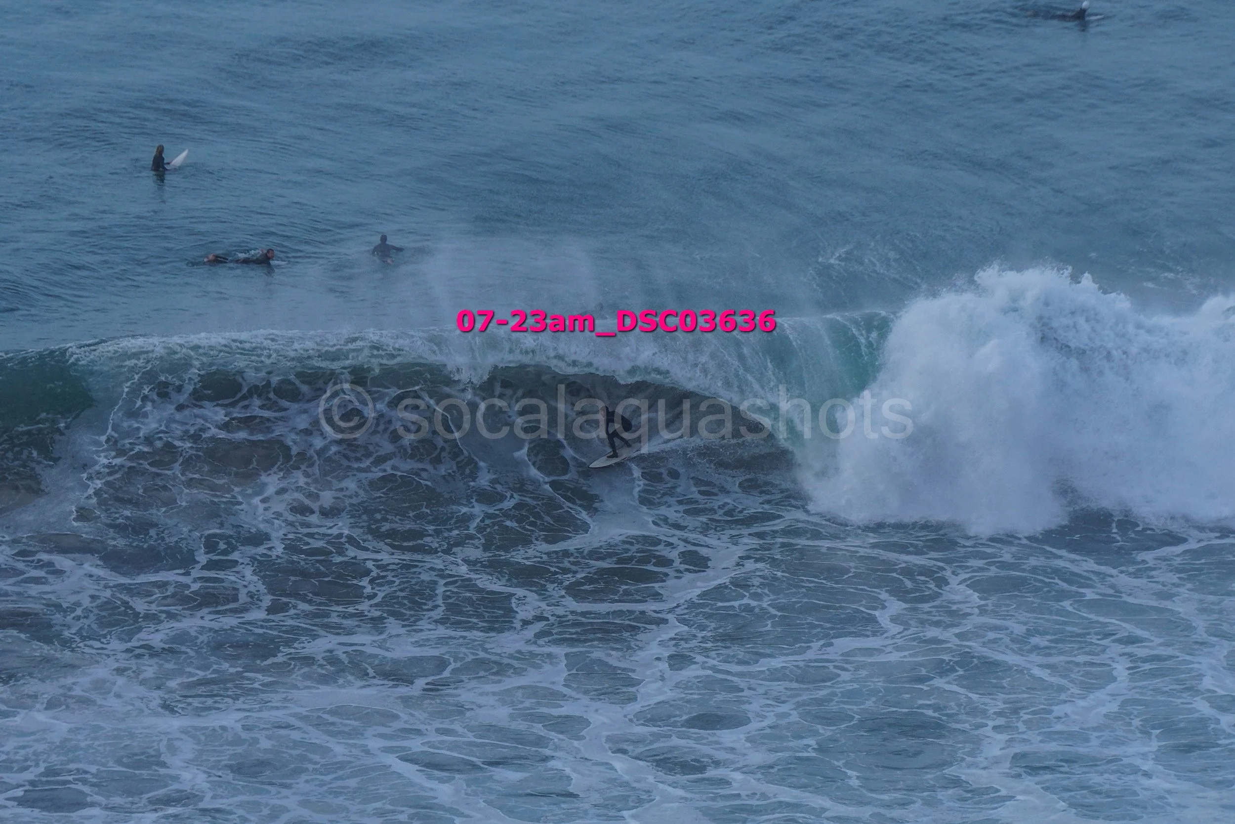 Surfer riding a wave with three people swimming or floating in the background in the ocean.