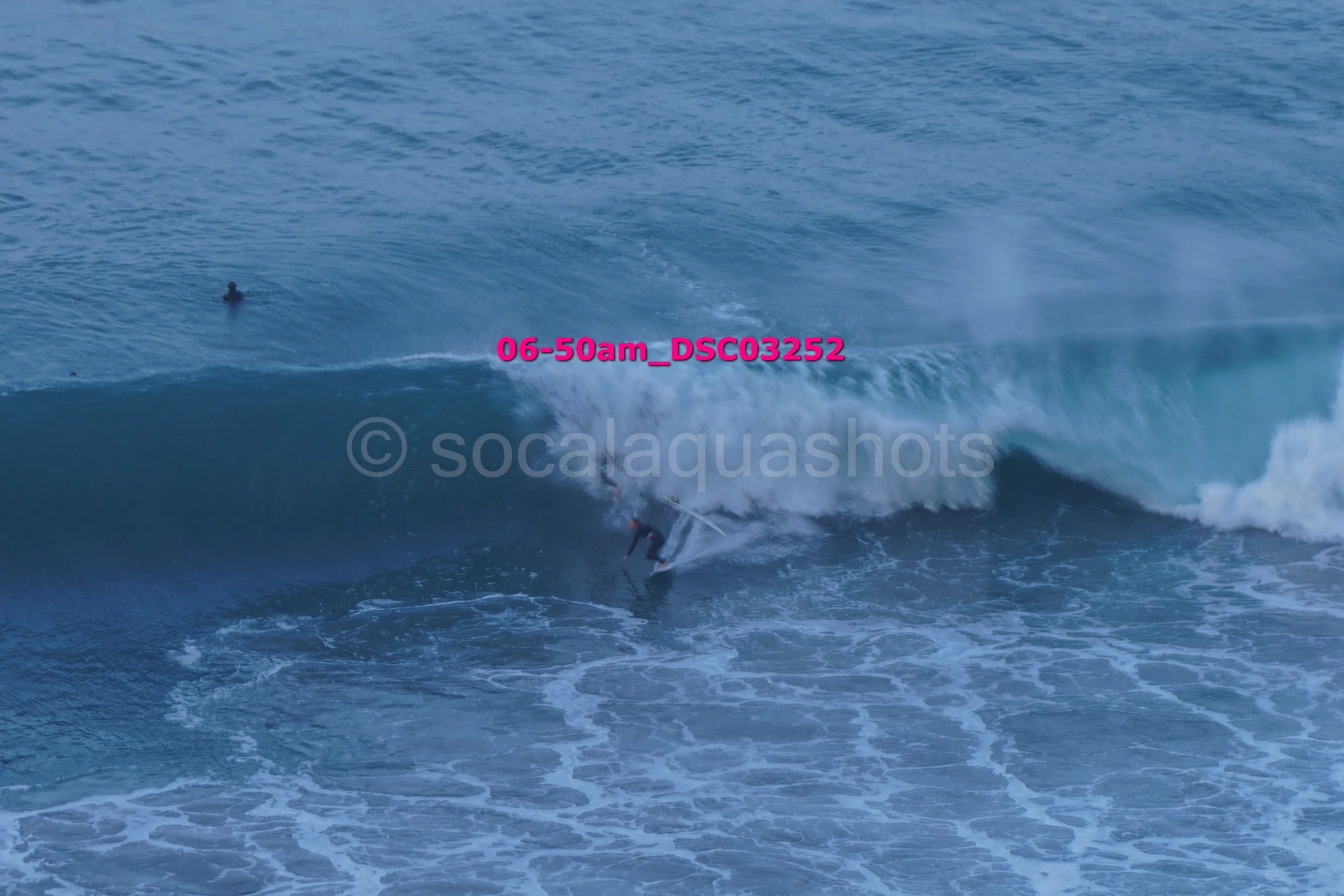 A person surfing on a large wave in the ocean at dawn.