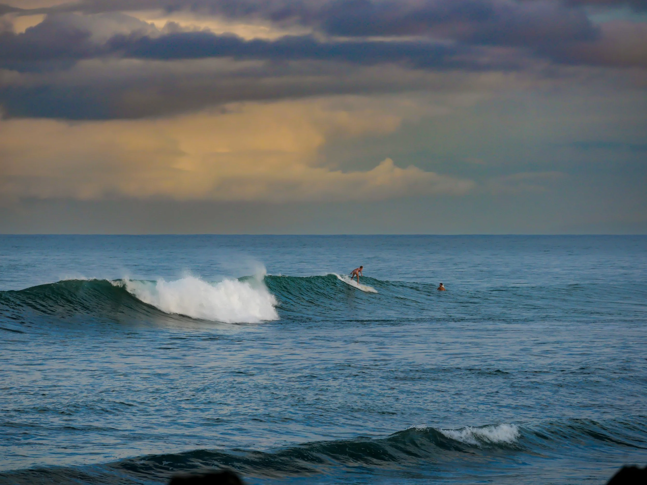 Surfer riding a wave in the ocean with cloudy sky