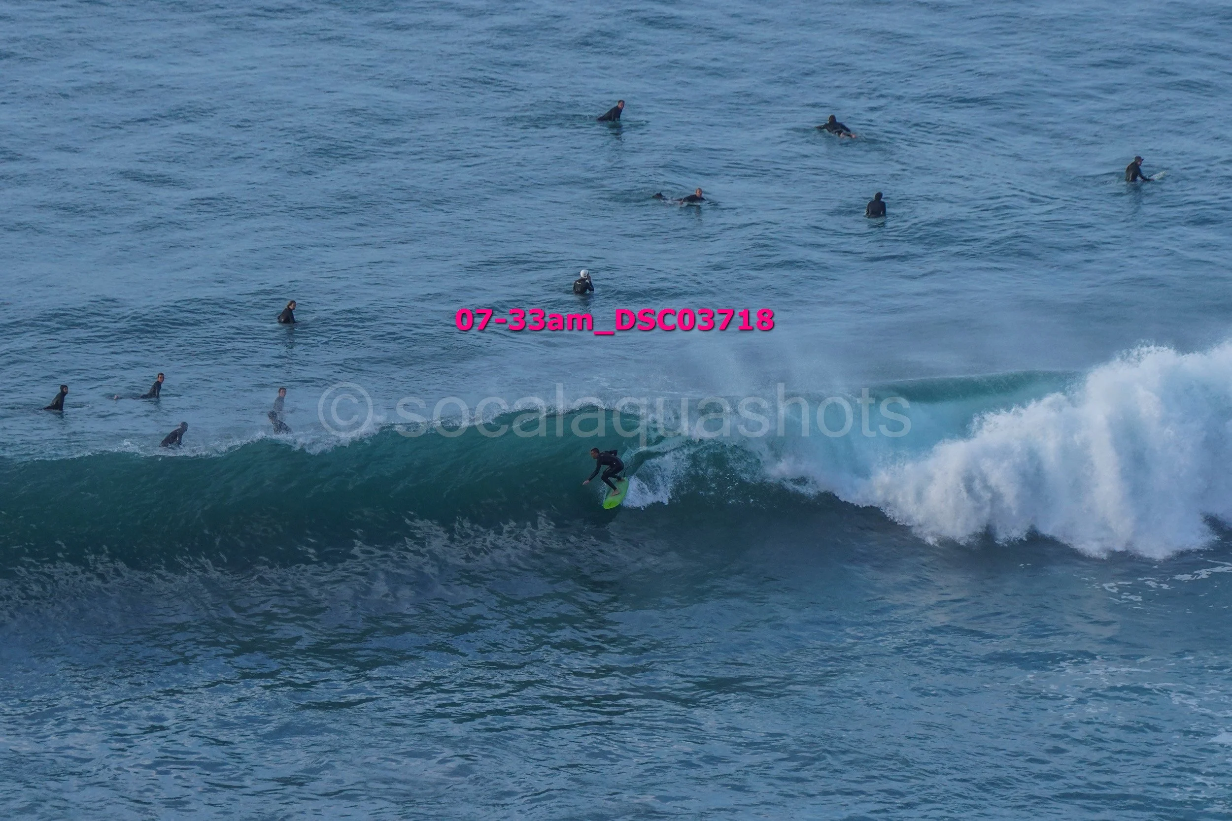 A person surfing on a wave with several others watching in the water.