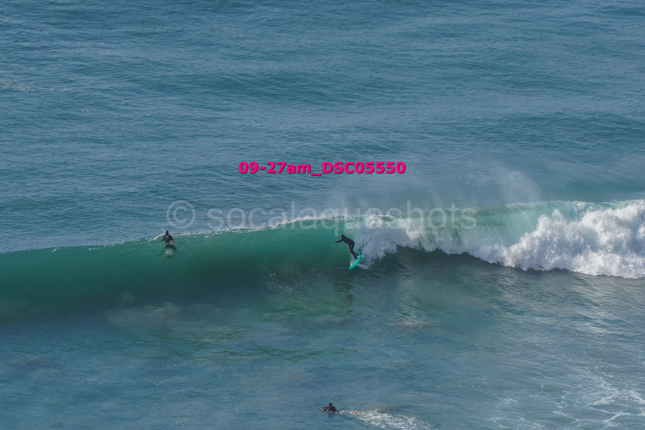 Two surfers riding a wave in the ocean, with a person swimming nearby.