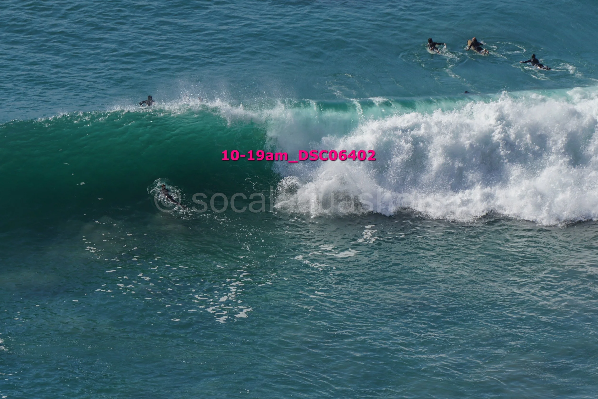 Surfers in the ocean riding and paddling on large ocean waves, with some submerged and others approaching the wave crest.
