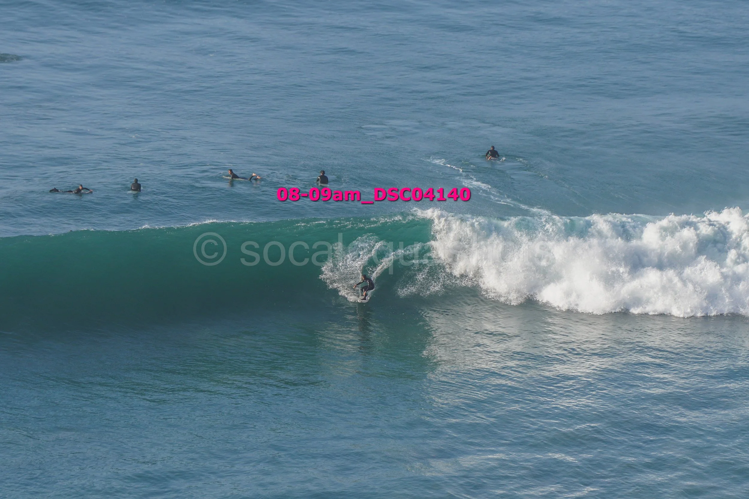 A person surfing a wave with five people in the water in the background at the beach.