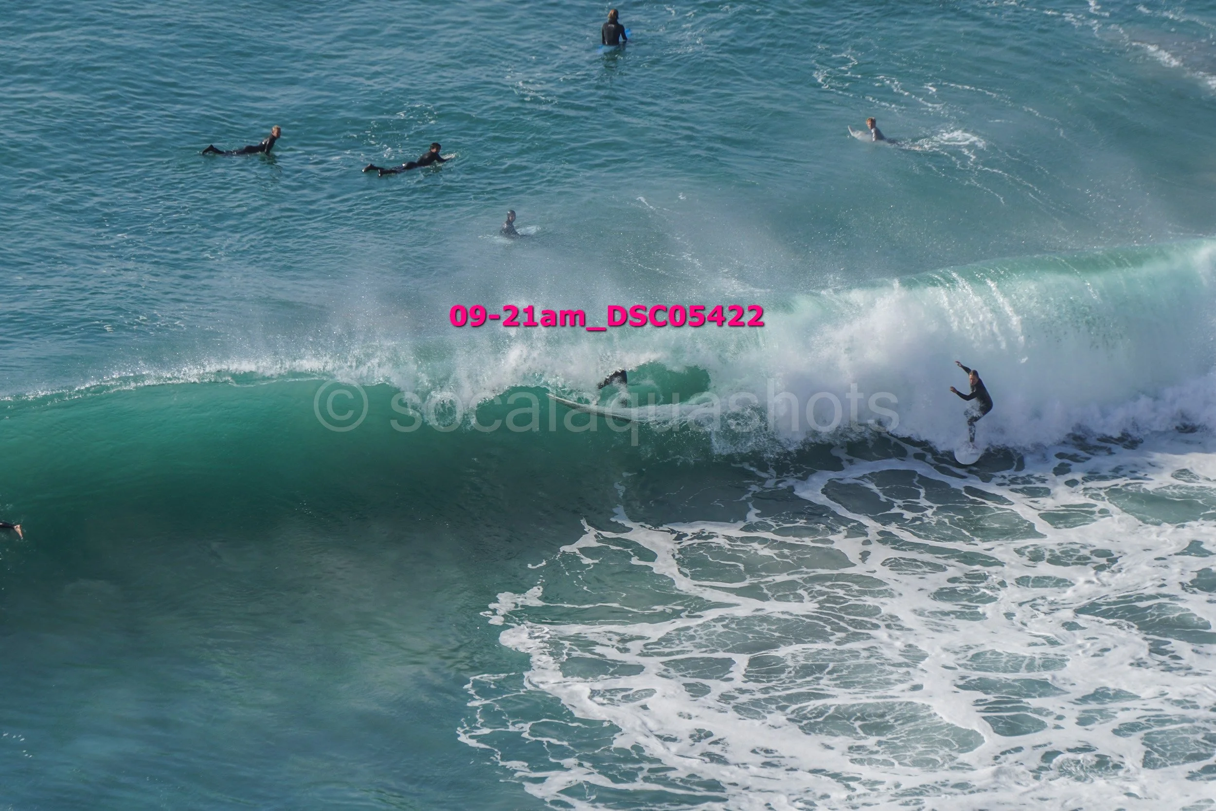 A surfer riding a large wave with several other surfers in the water nearby.