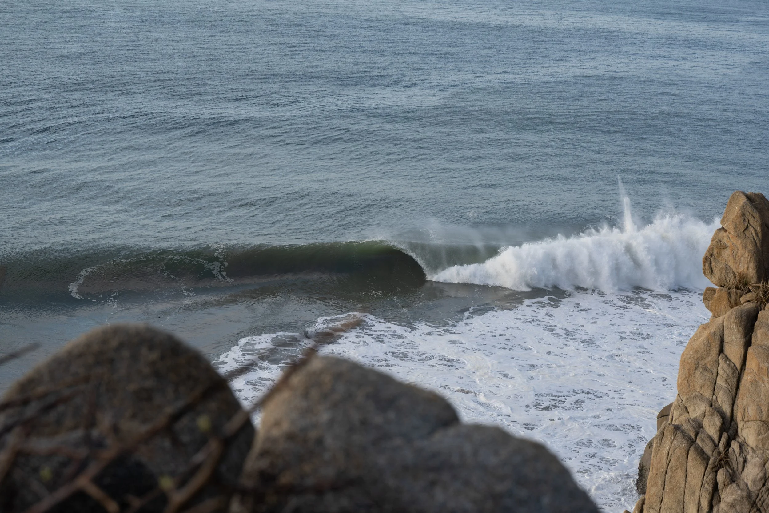 Ocean waves crashing against rocks with a rocky shoreline in the foreground.