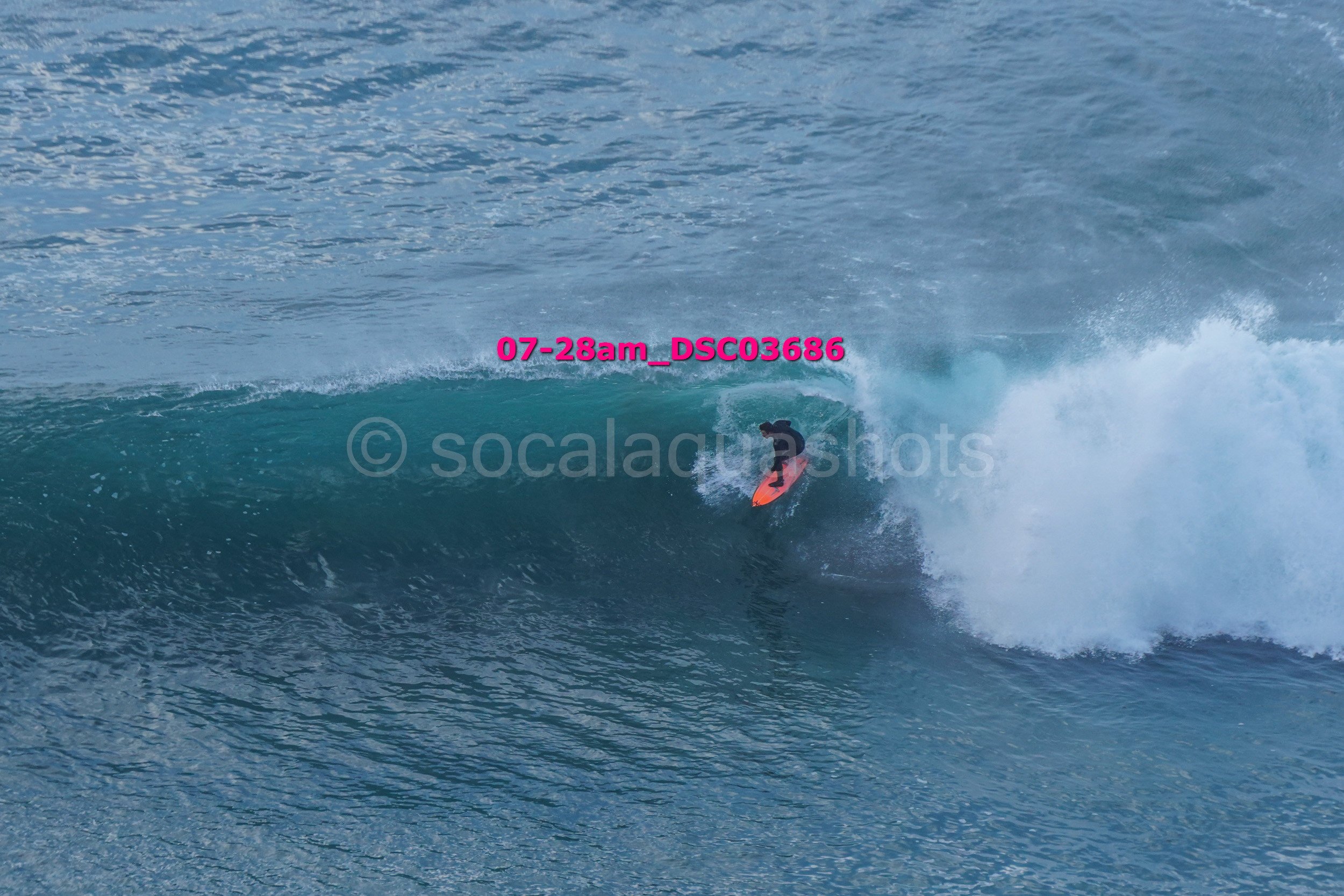 A person surfing on a large ocean wave, wearing a black wetsuit with a bright orange surfboard.