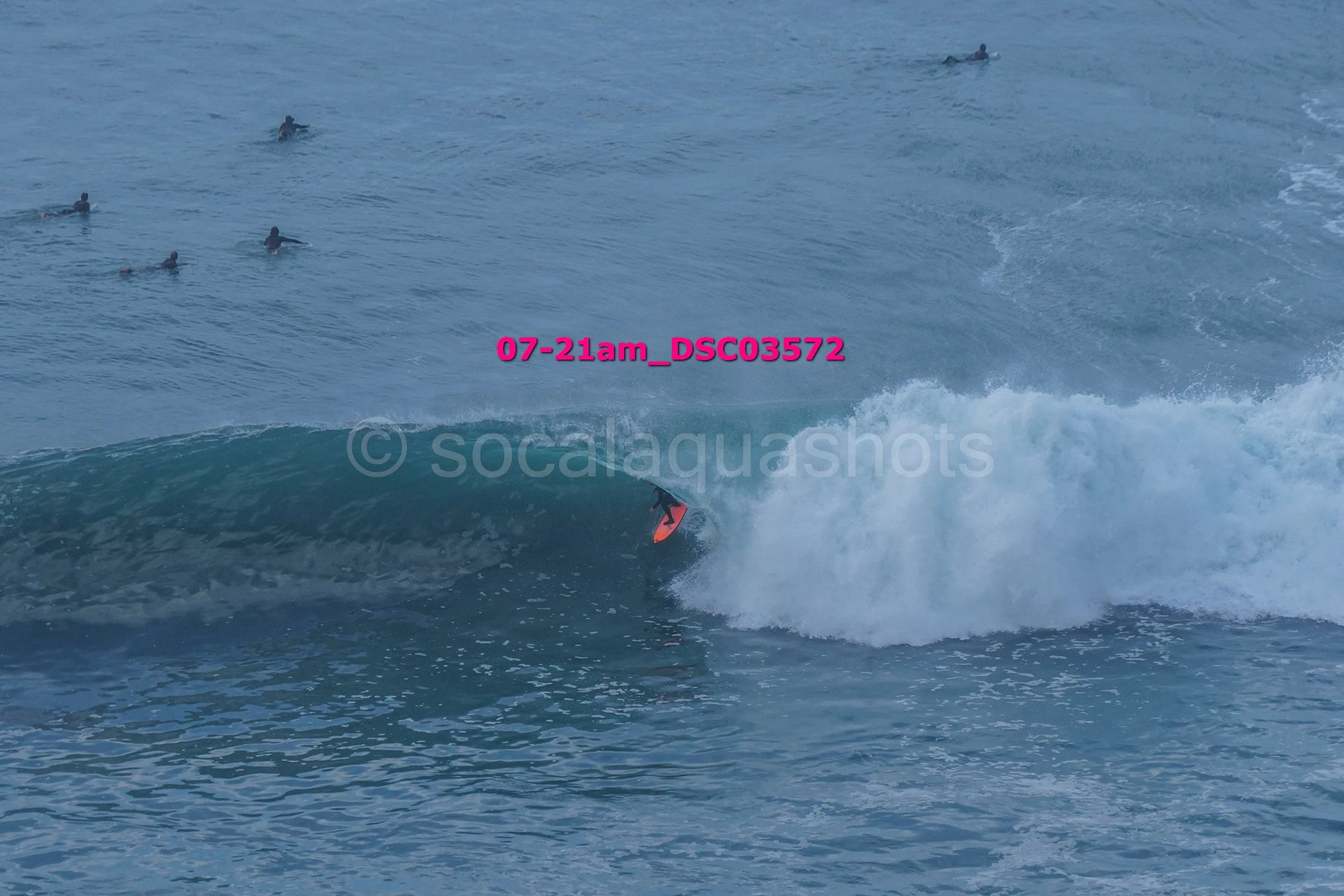 A person surfing a wave in the ocean with several people swimming in the background.
