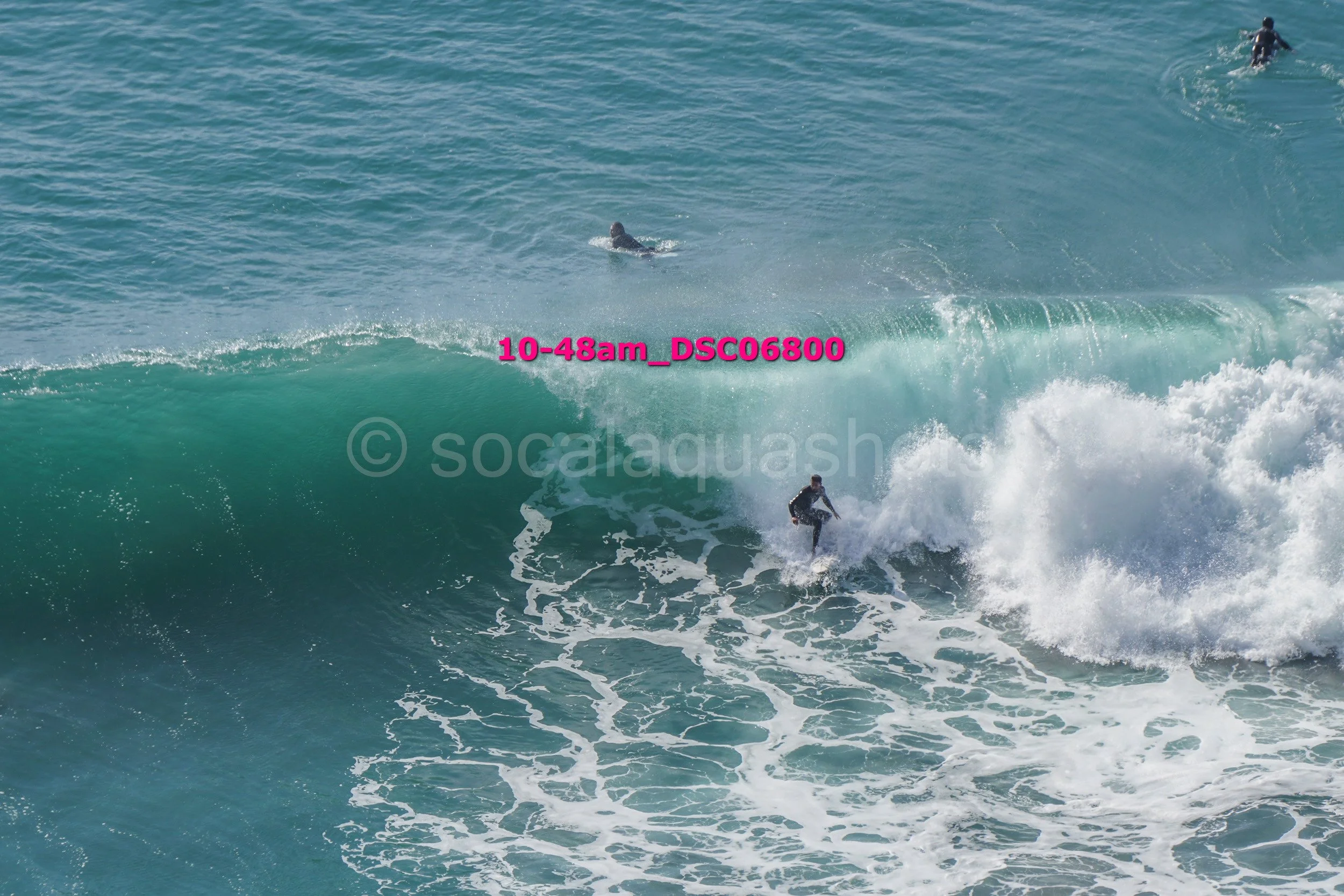 Surfer riding a wave with several people swimming in the background in the ocean.