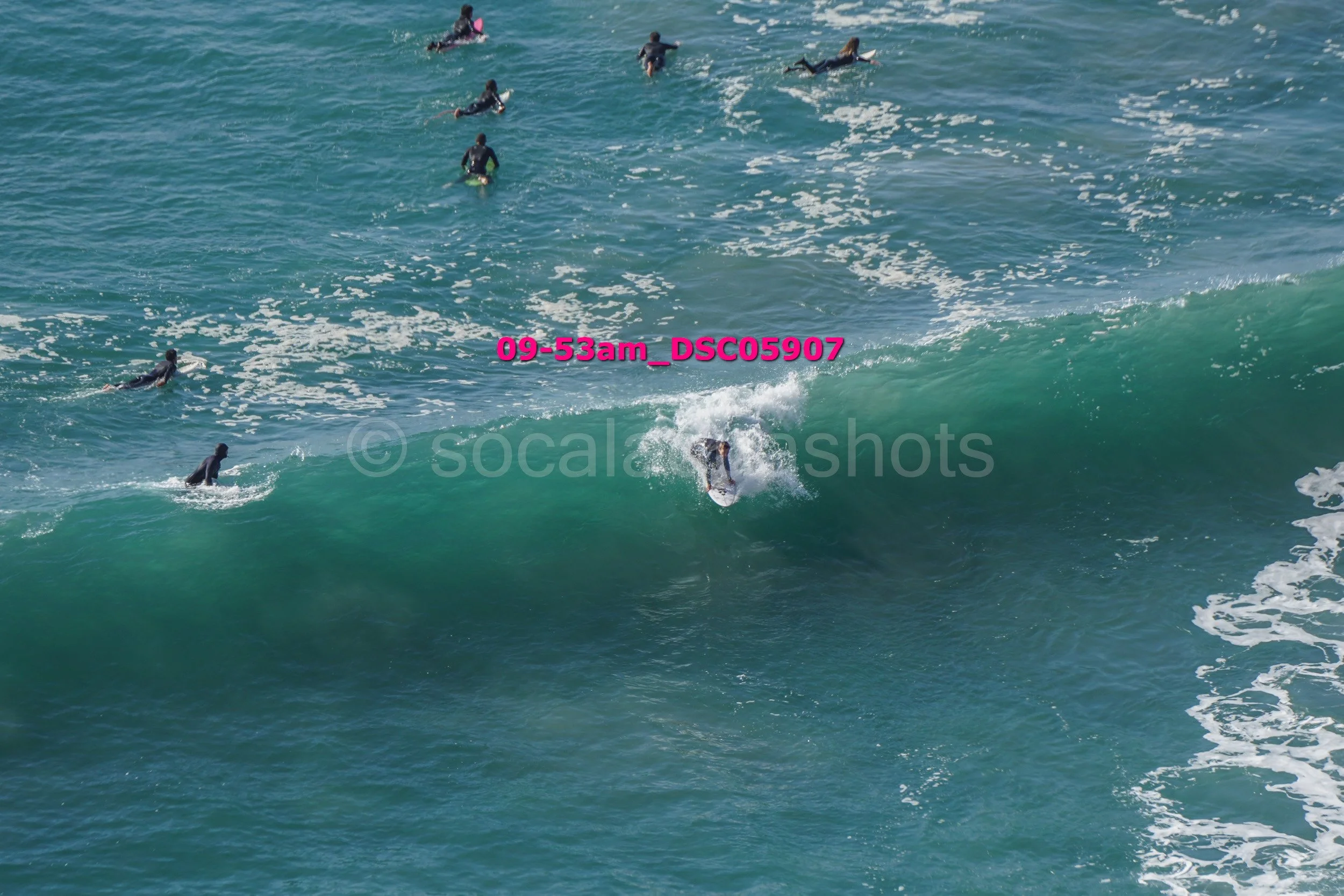 A person surfing on a large wave with multiple other surfers in the water nearby.