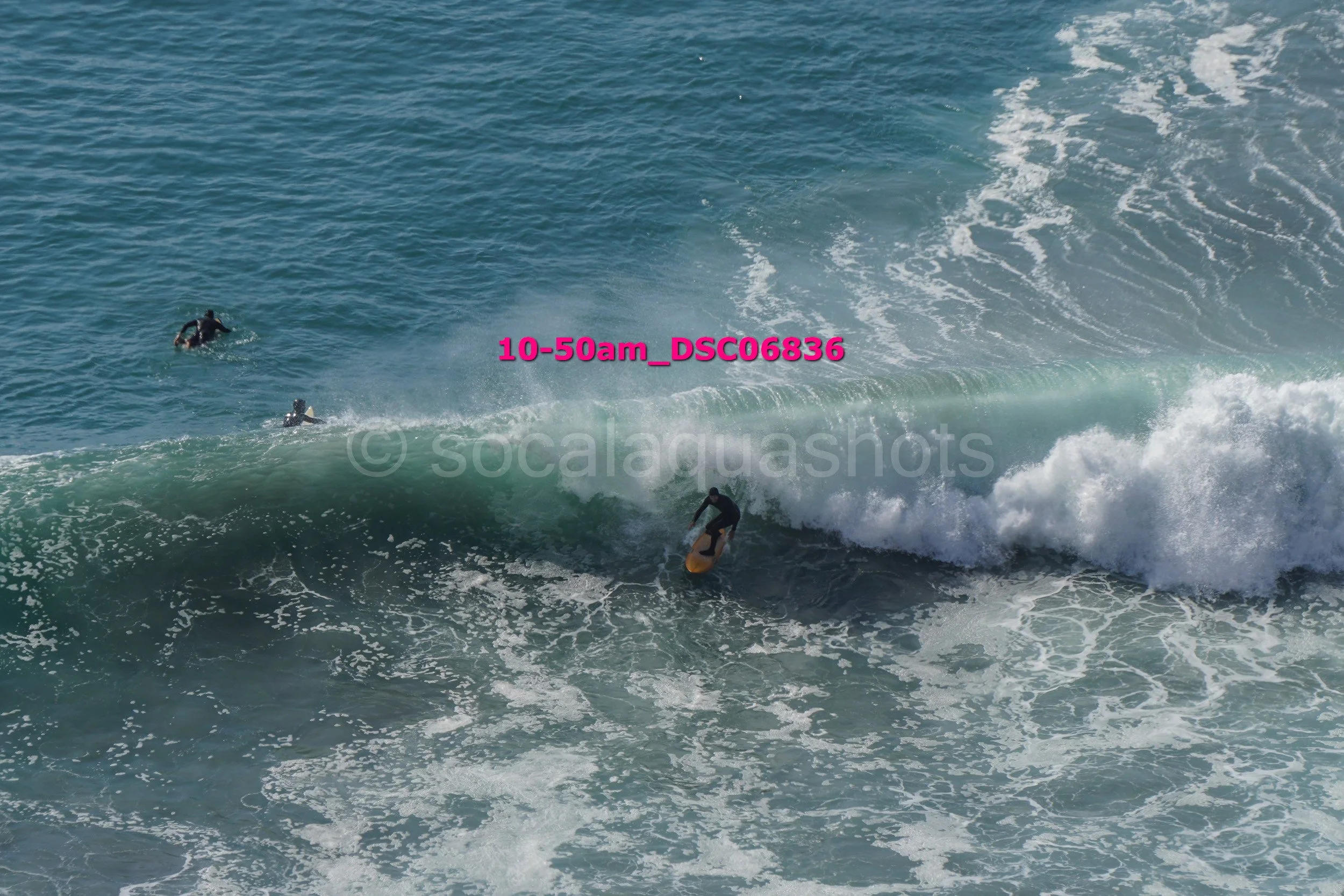 Surfer riding a wave in the ocean with two other surfers in the water nearby.