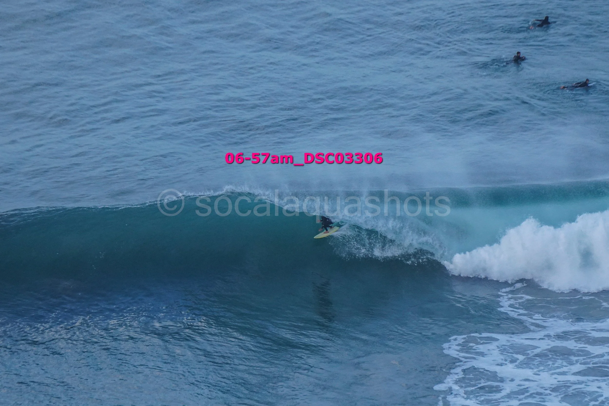 Surfer riding a wave in the ocean, with several other surfers visible in the background.