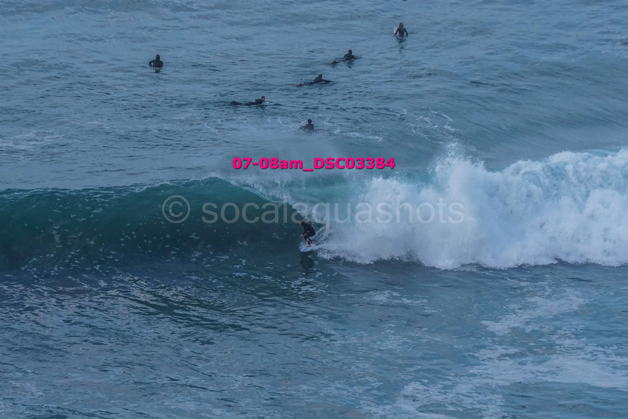 A surfer riding a wave with multiple surfers in the water watching nearby.