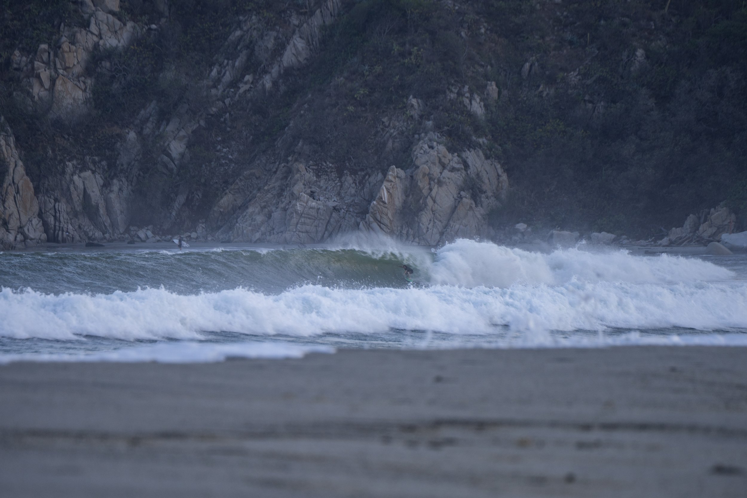 Waves crashing on the shore with rocky cliffs and forested hillside in the background