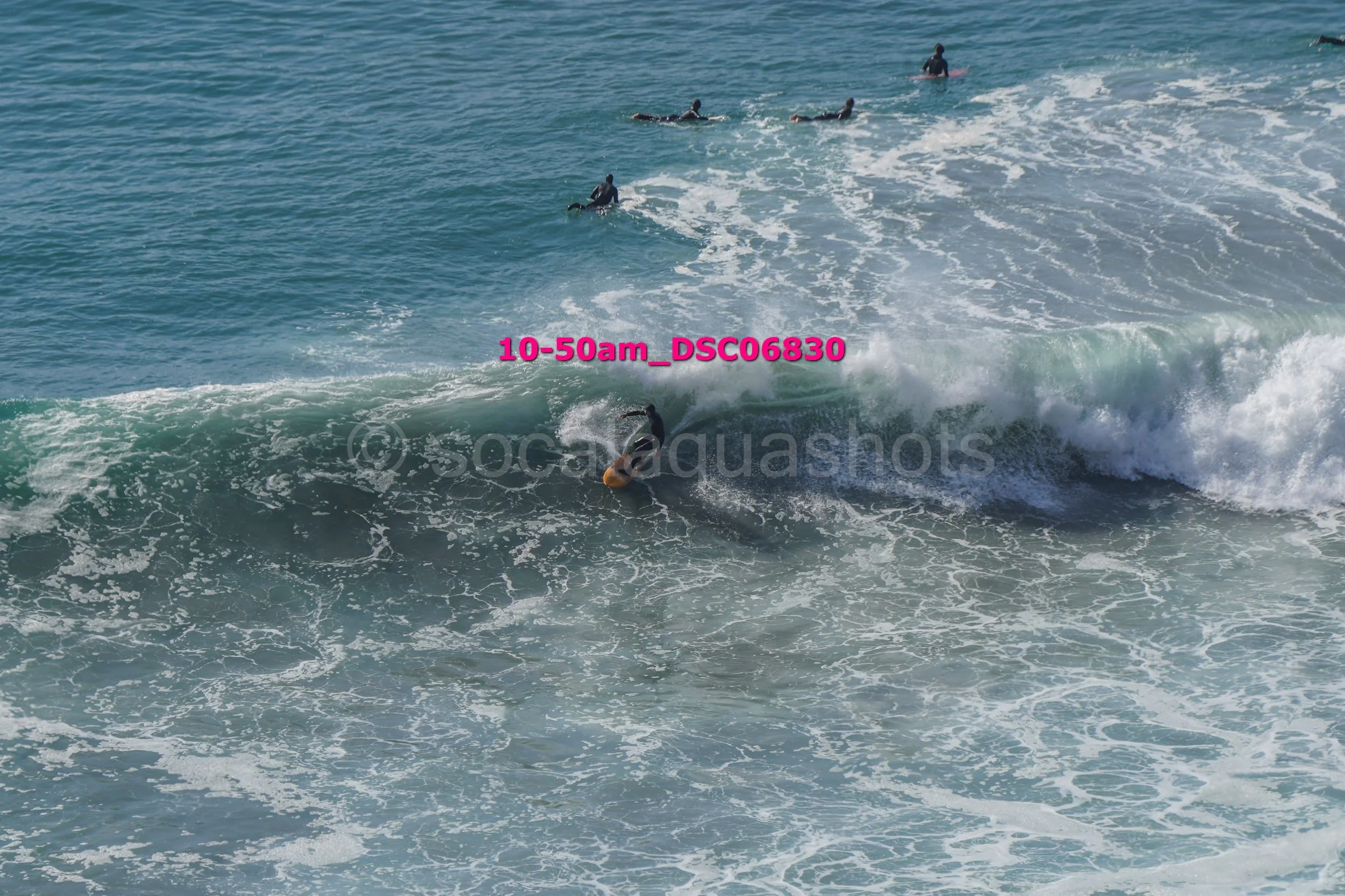 A person surfing a wave in the ocean with several other surfers in the background.