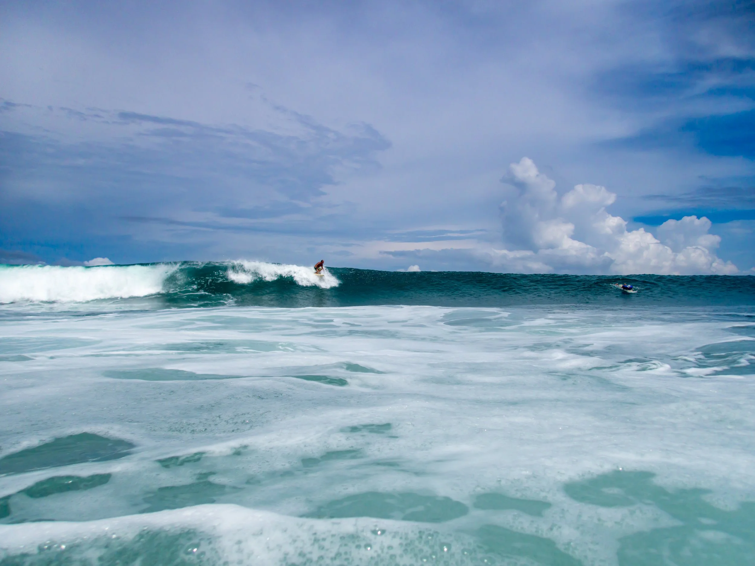 Surfer riding a wave in the ocean under a cloudy sky