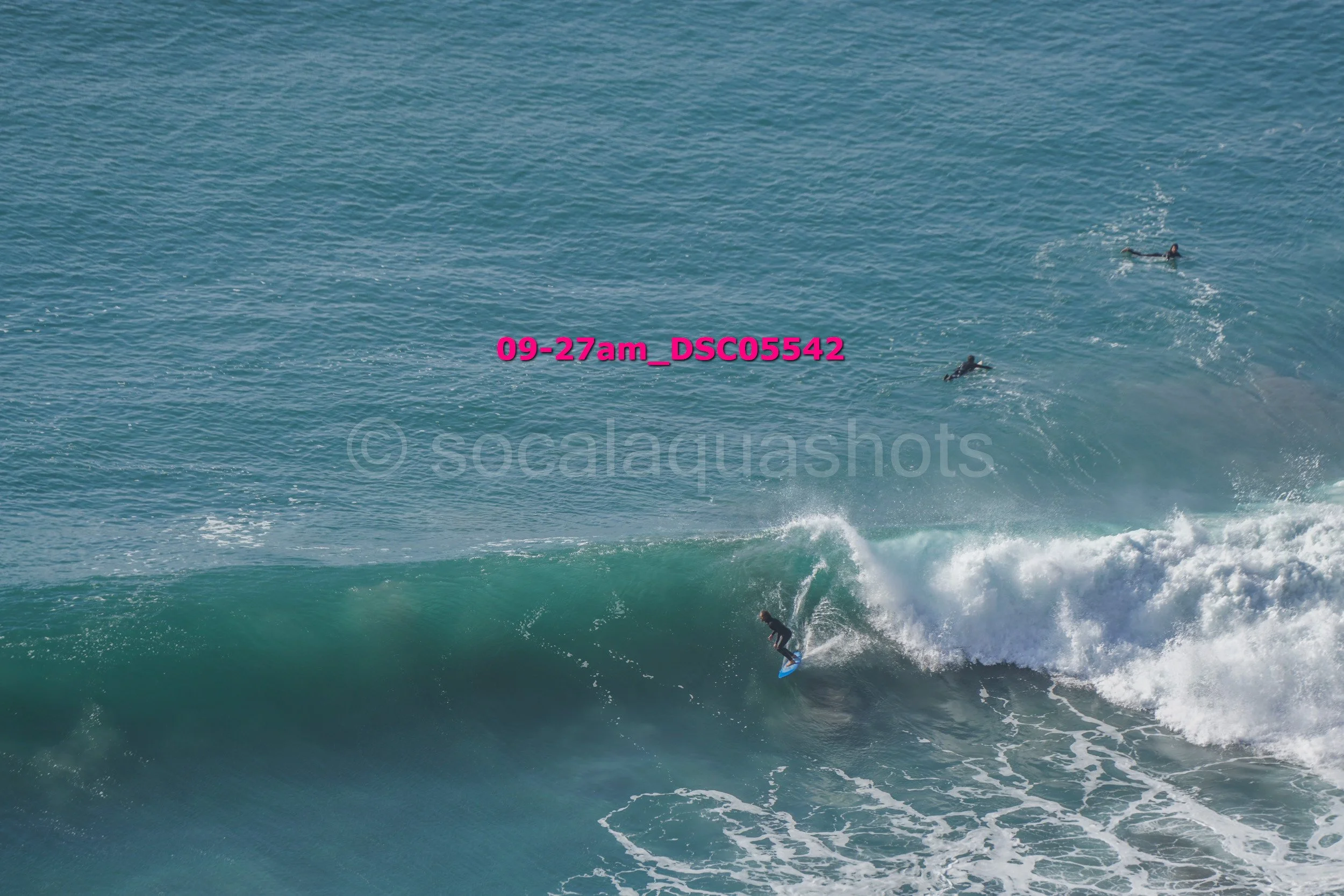 A person surfing on a wave in the ocean with two other surfers swimming in the distance.