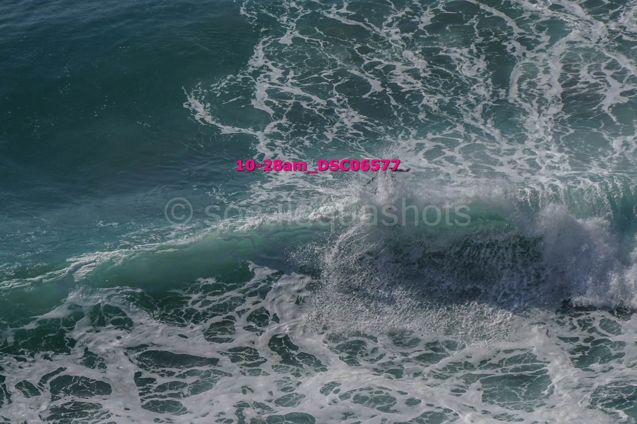 Aerial view of ocean waves crashing with visible foam and a surfboard submerged in the water.