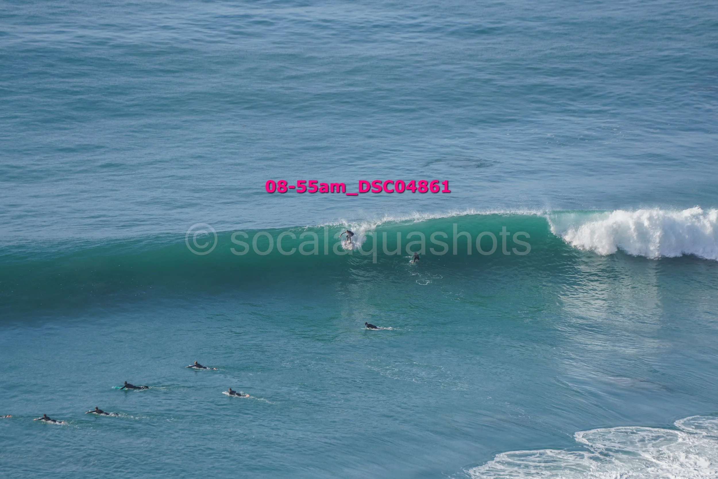 Multiple surfers riding a large ocean wave, with some paddling in the water.